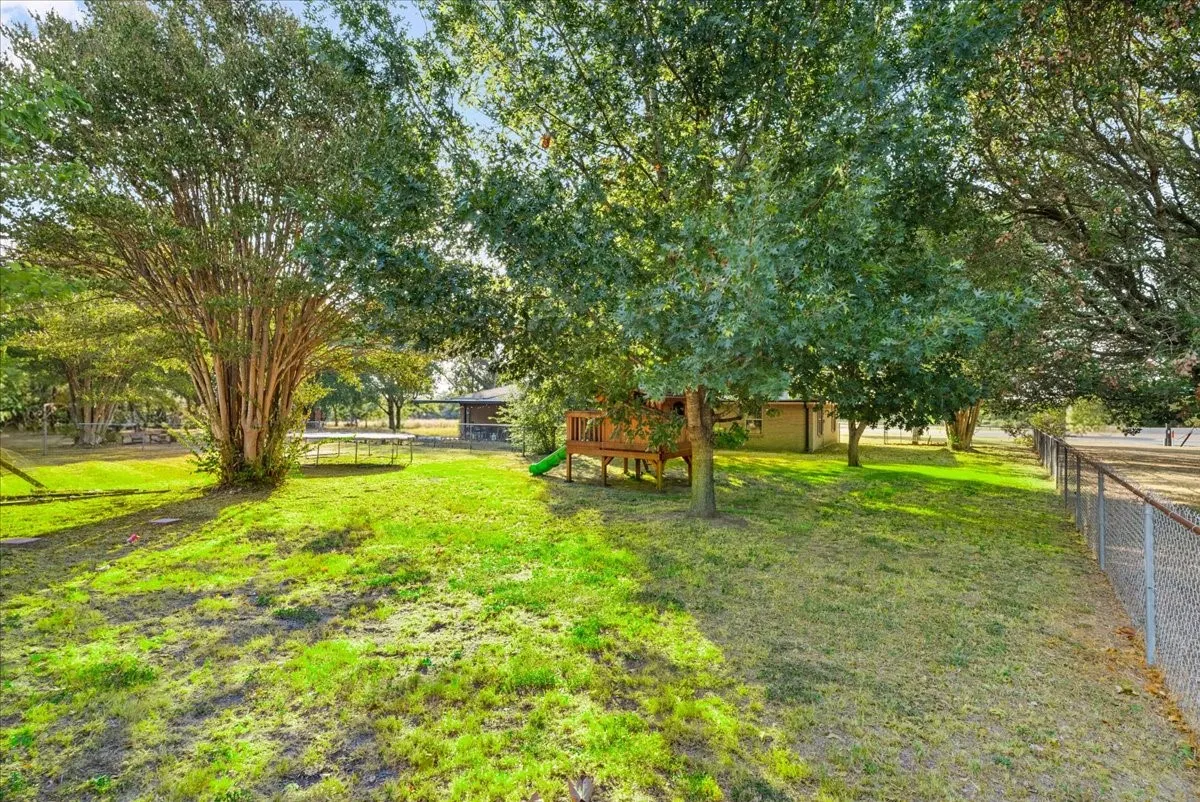 Expansive grassy yard with mature trees and a chain-link fence