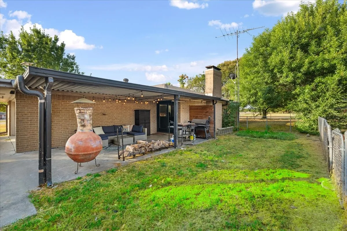 Expansive backyard featuring a covered patio, brick exterior, and a prominent chimney