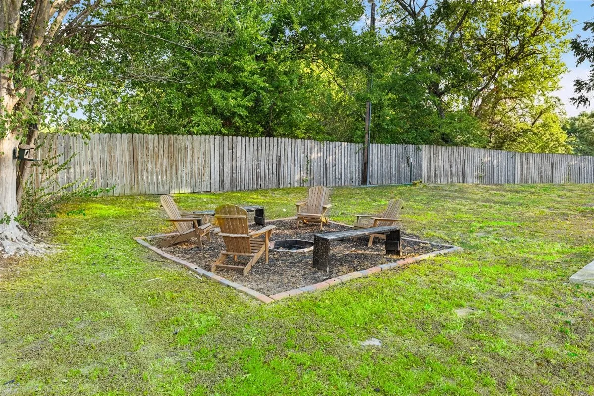 Expansive backyard featuring a wood privacy fence, established trees, and a dedicated fire pit area
