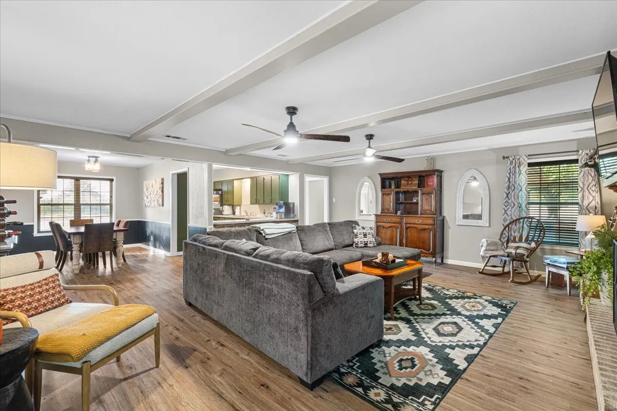 Expansive living area with wood-finish flooring, exposed ceiling beams, and dual ceiling fans