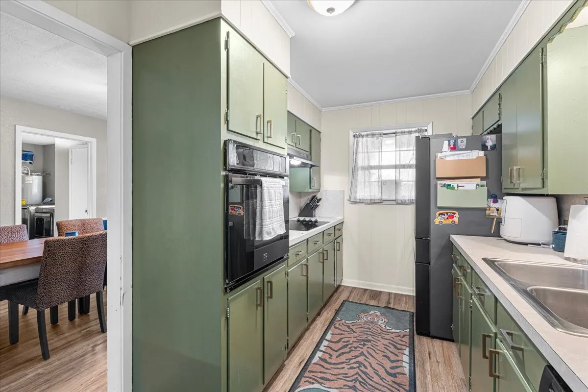 Galley kitchen with wood-finish flooring, paneled walls, extensive cabinetry, built-in double ovens, and a window
