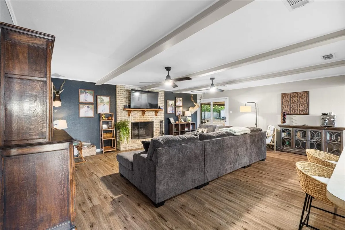 Wood-finish flooring, exposed ceiling beams, and a brick fireplace with a wood mantle