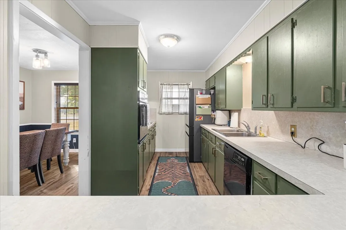Galley kitchen featuring wood-finish flooring, light-colored countertops, dark green cabinetry, and stainless steel appliances