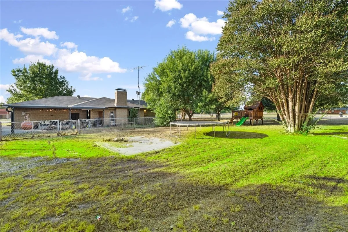 Expansive green lawn with mature trees and a brick exterior residence featuring a chimney