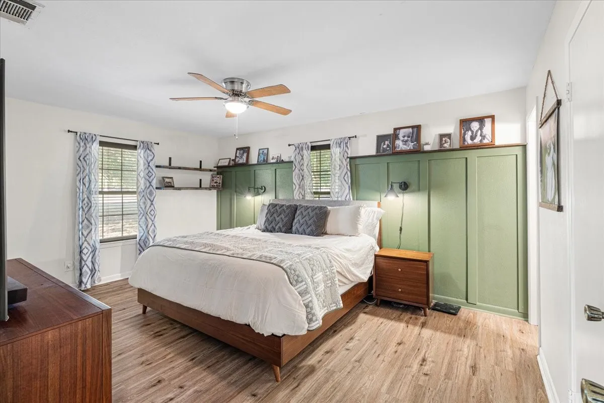 Wood-finish flooring, a ceiling fan with integrated lighting, two windows, and built-in shelving
