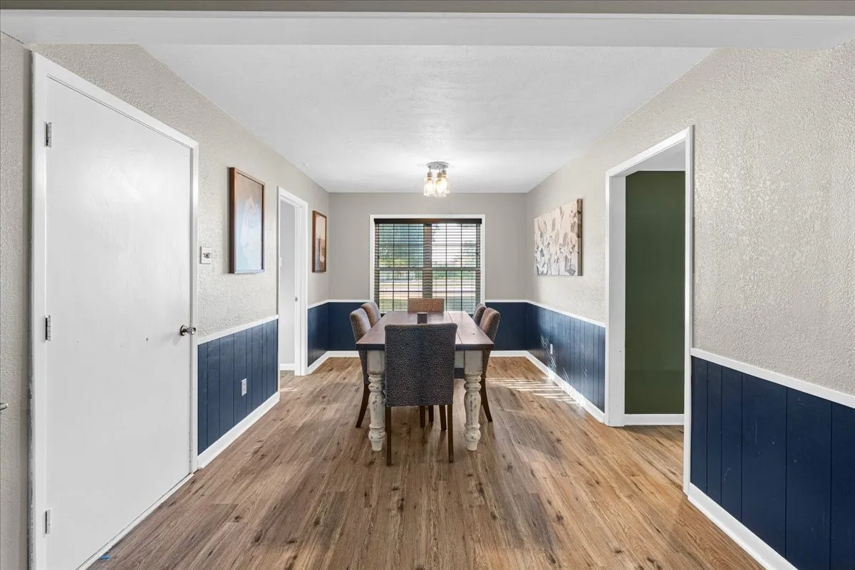 Wood-finish flooring, half-wall paneling, window with horizontal blinds, and a built-in ceiling light fixture