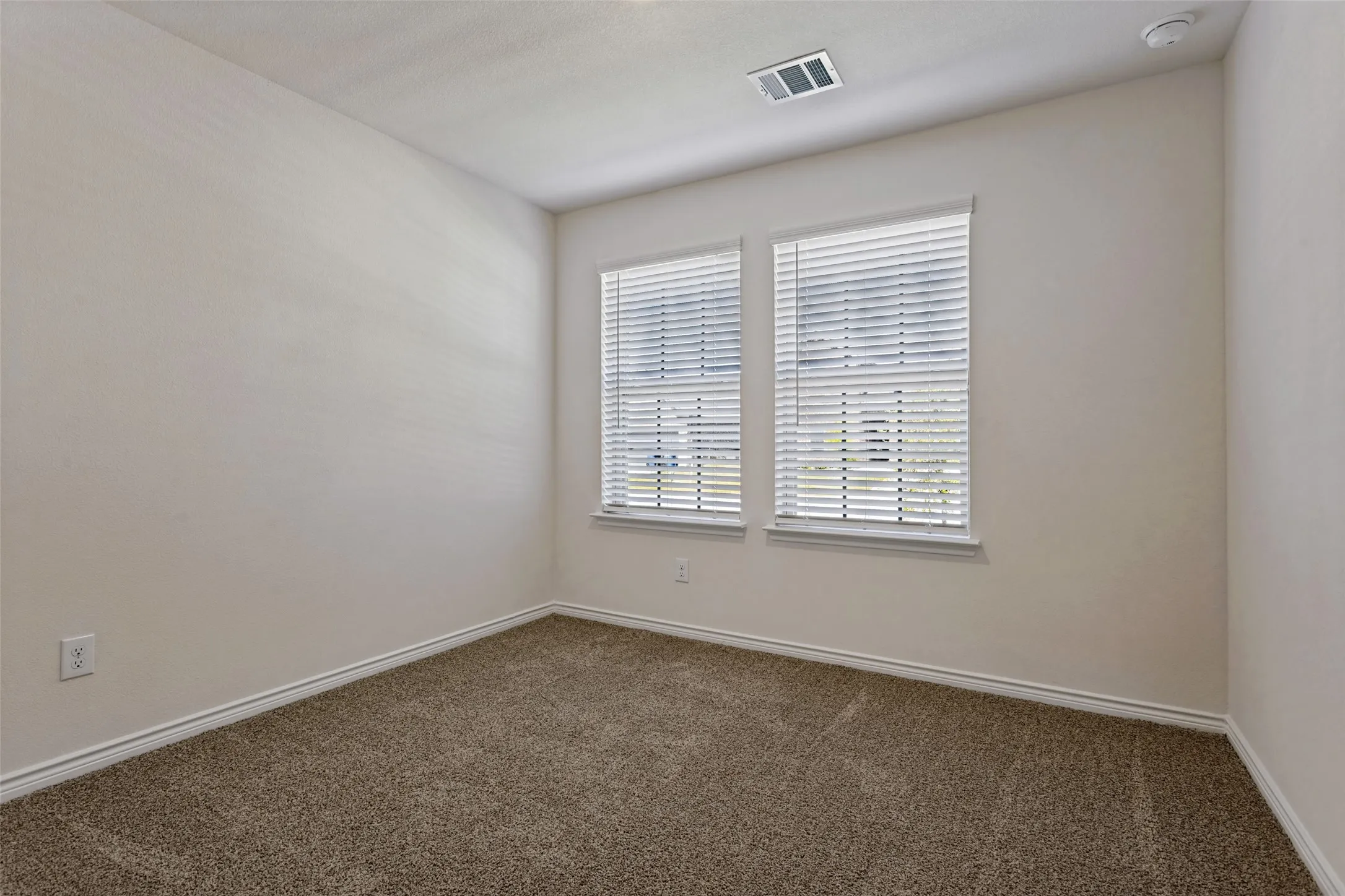 Neutral wall paint, plush carpet flooring, two windows with blinds, and white trim