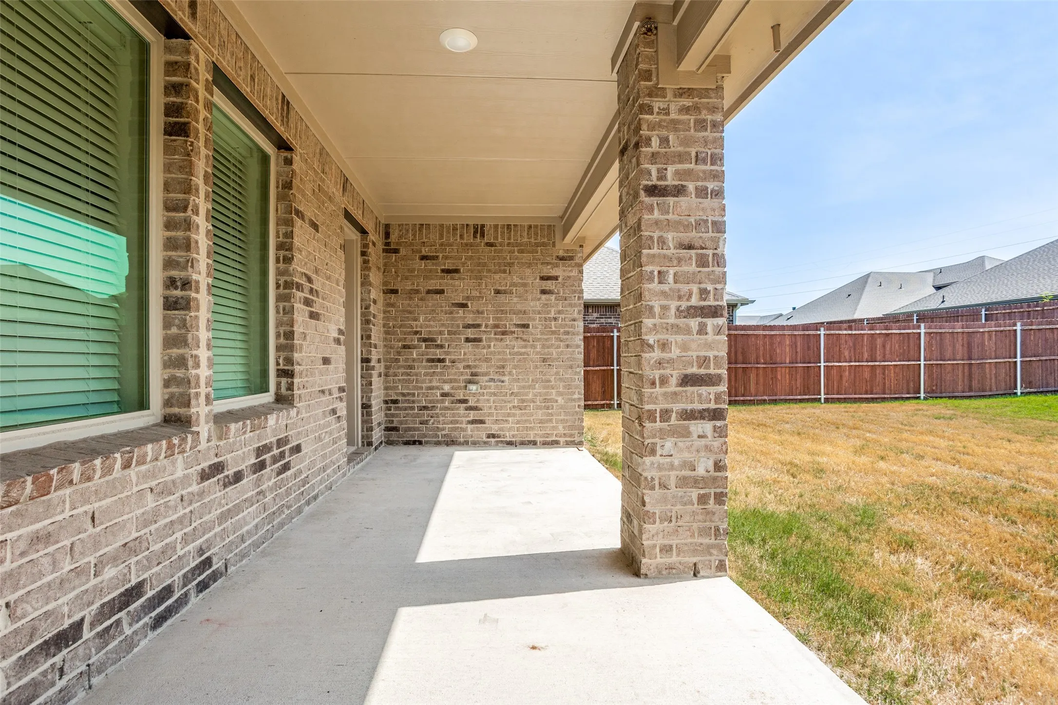 Covered concrete patio with recessed lighting, brick exterior, and a fenced perimeter