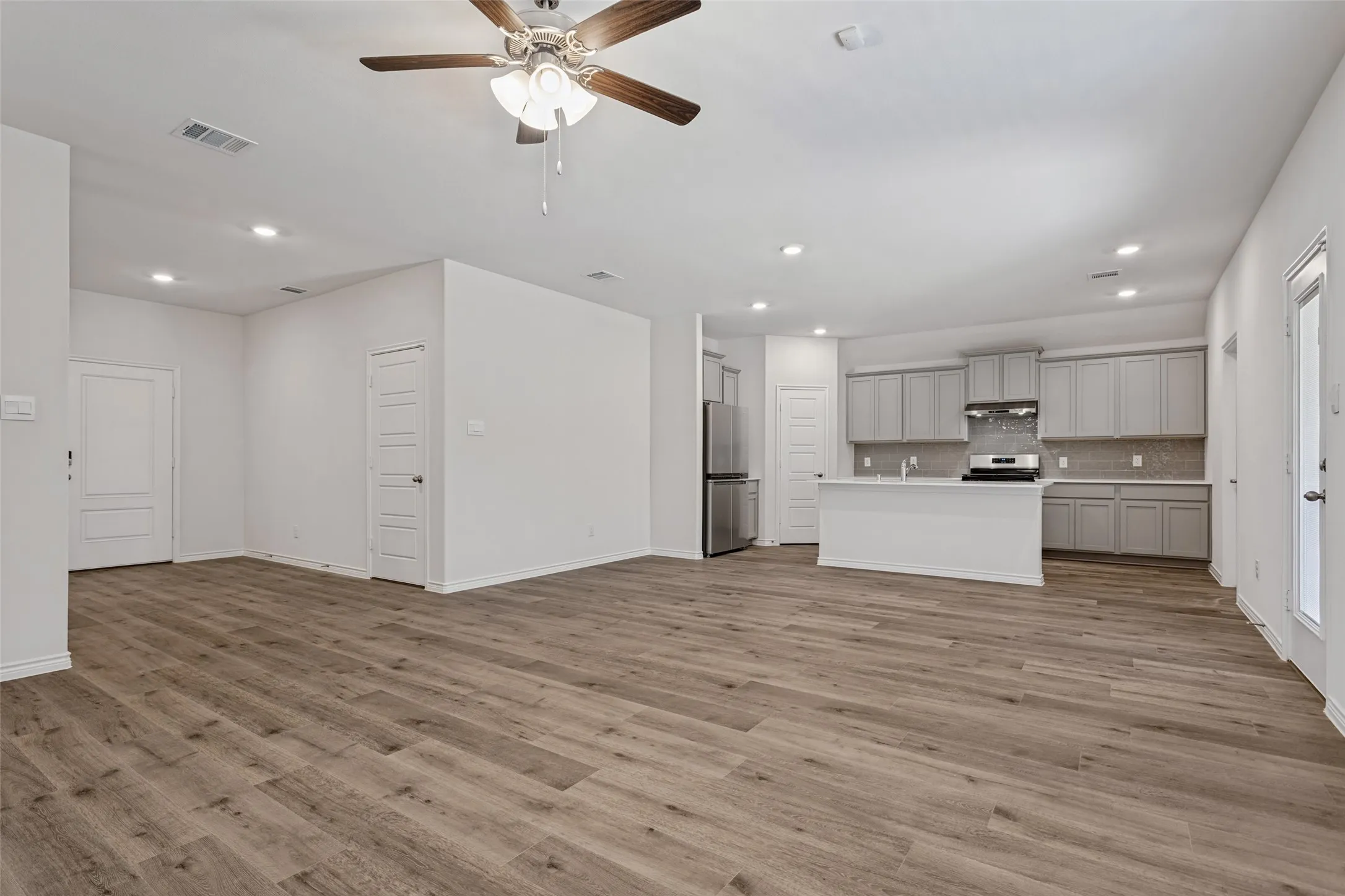 Wood-finish flooring throughout, recessed lighting, ceiling fan, grey shaker-style cabinetry, and stainless steel appliances