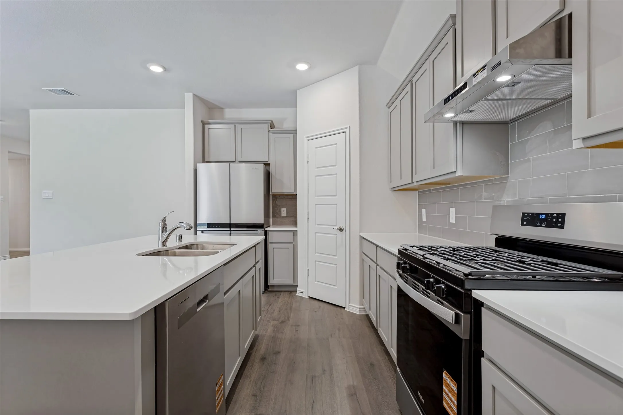 Kitchen featuring a stainless steel range, coordinating stainless steel refrigerator, light gray cabinetry, light countertops, and wood-finish flooring