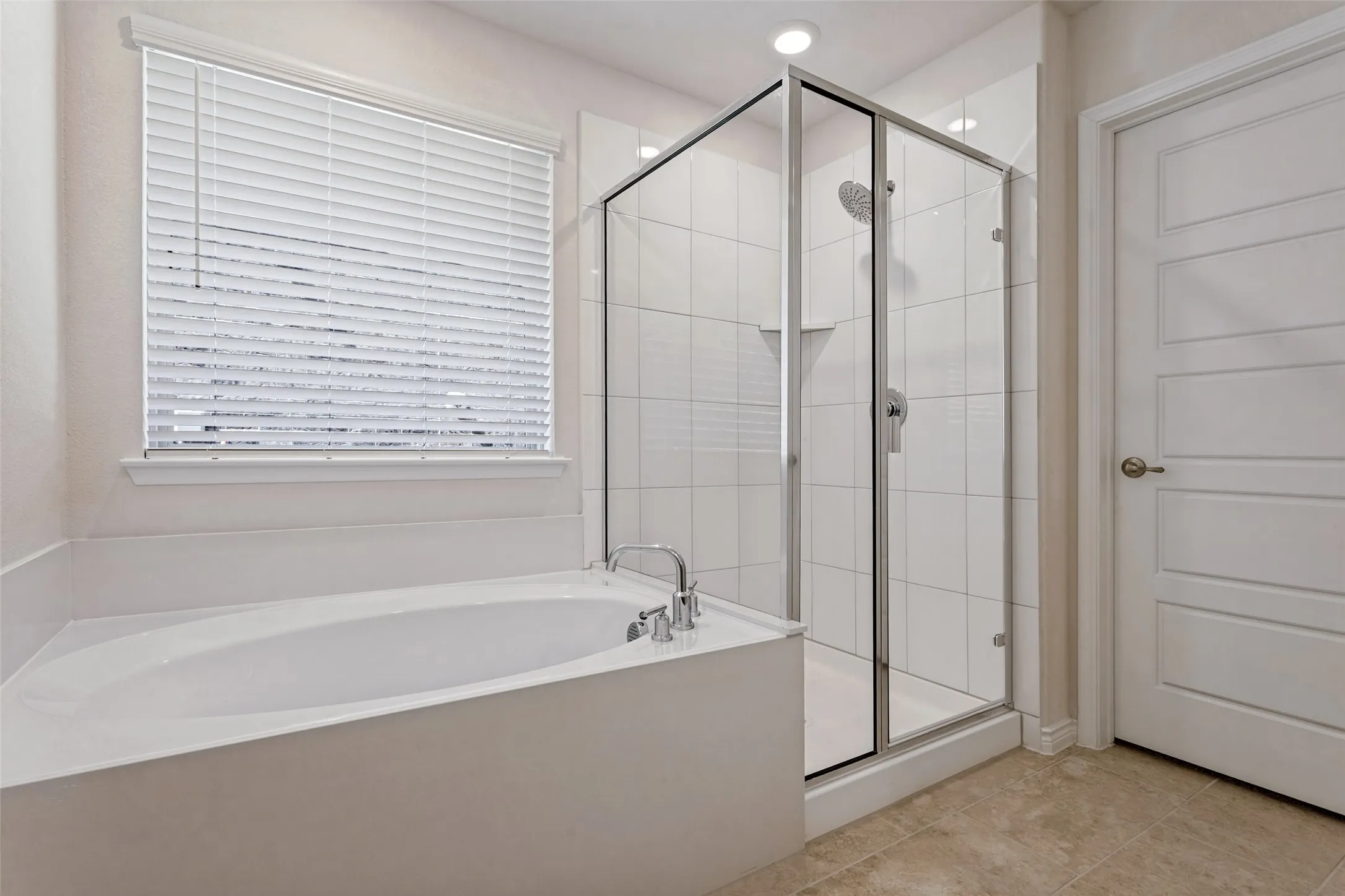 Soaking tub with deck-mounted faucet, walk-in shower with glass enclosure, white tile surround, and neutral tile flooring