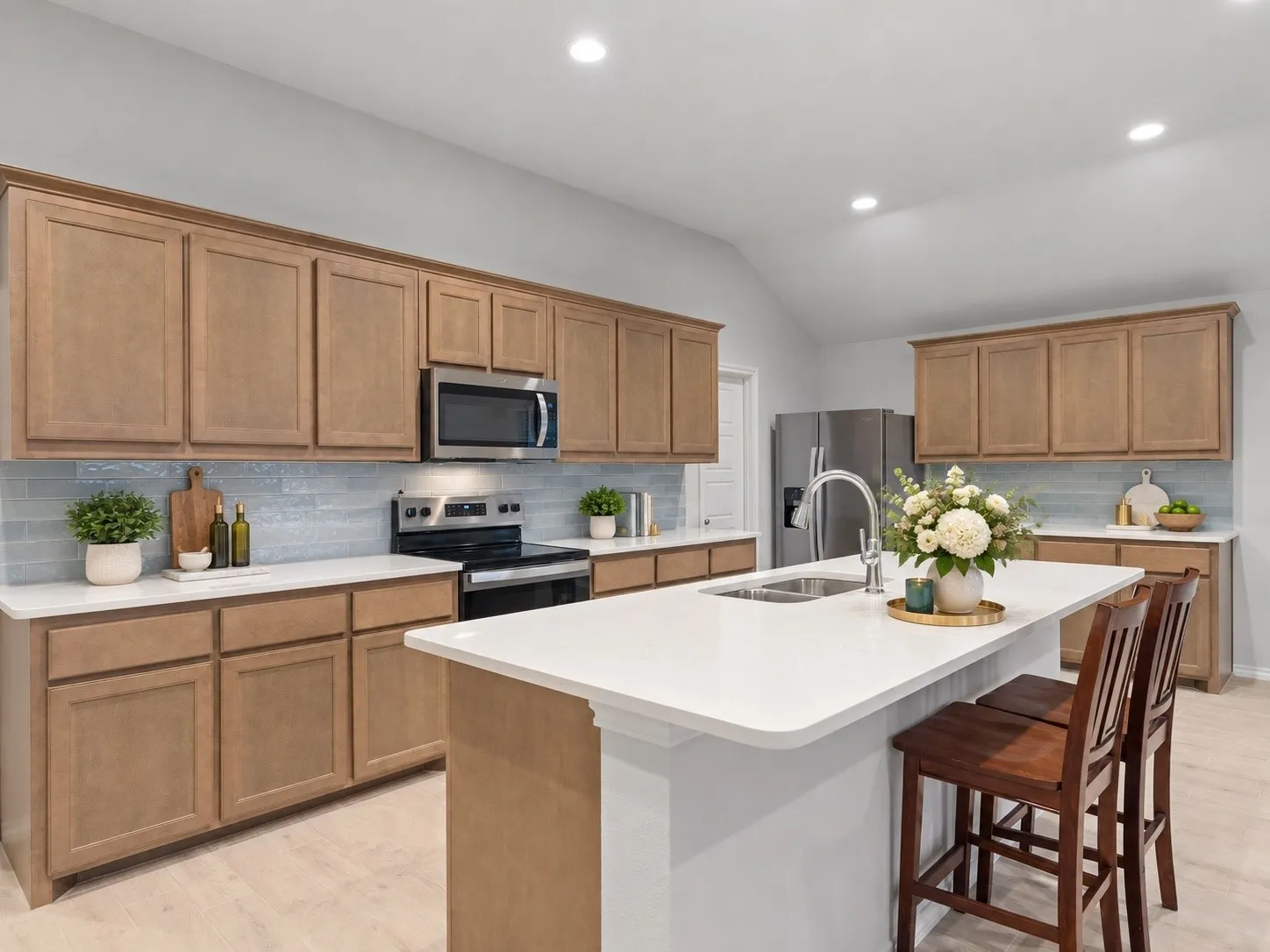 Spacious kitchen featuring light wood-finish cabinetry, light blue tile backsplash, stainless steel appliances, and a central island with a sink and seating