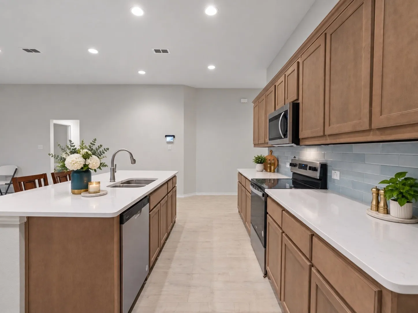 Kitchen featuring wood-finish cabinetry, stainless steel appliances, a center island with sink, white countertops, and a blue subway tile backsplash