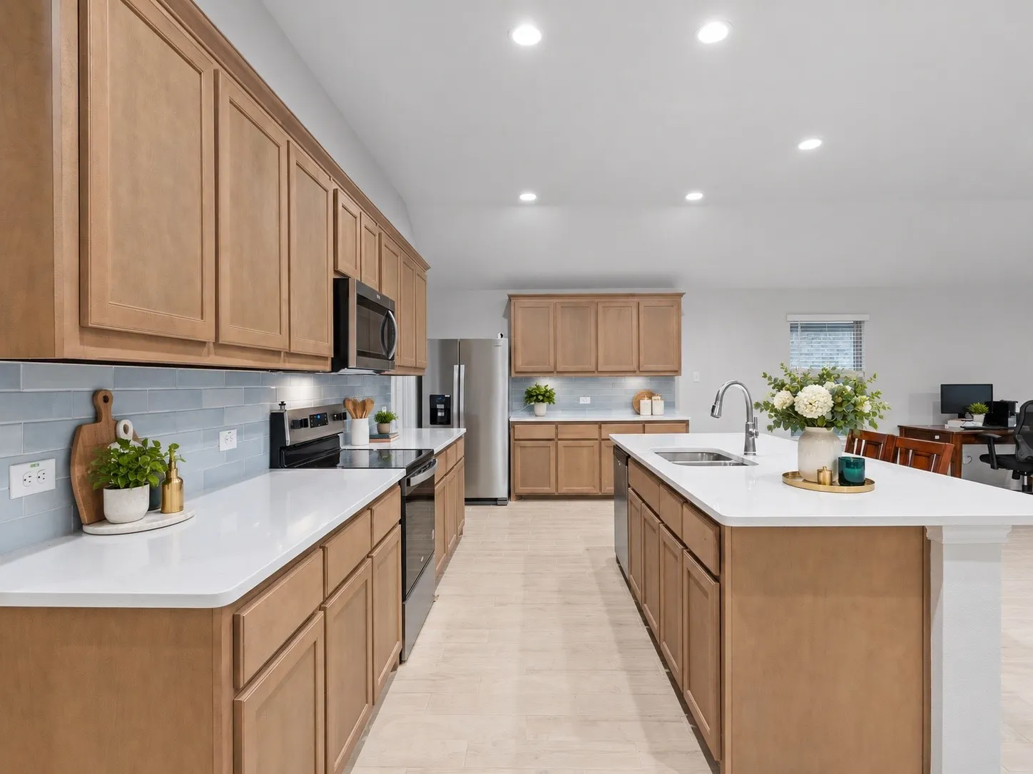 Kitchen featuring wood-finish cabinetry, light-toned countertops, a central island with an integrated sink, stainless steel appliances, and a tiled backsplash