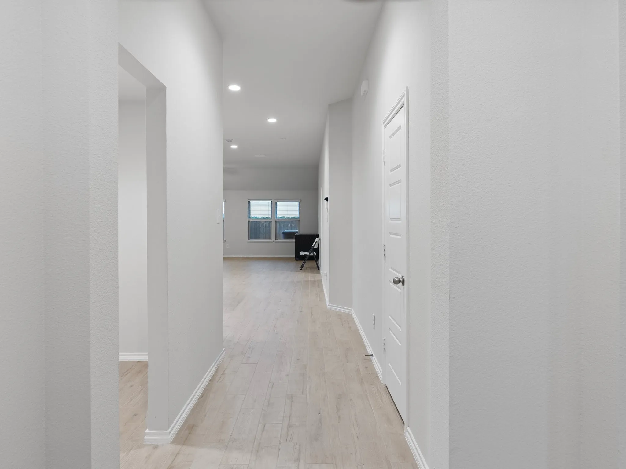 Recessed lighting illuminates the hallway with light wood-finish flooring