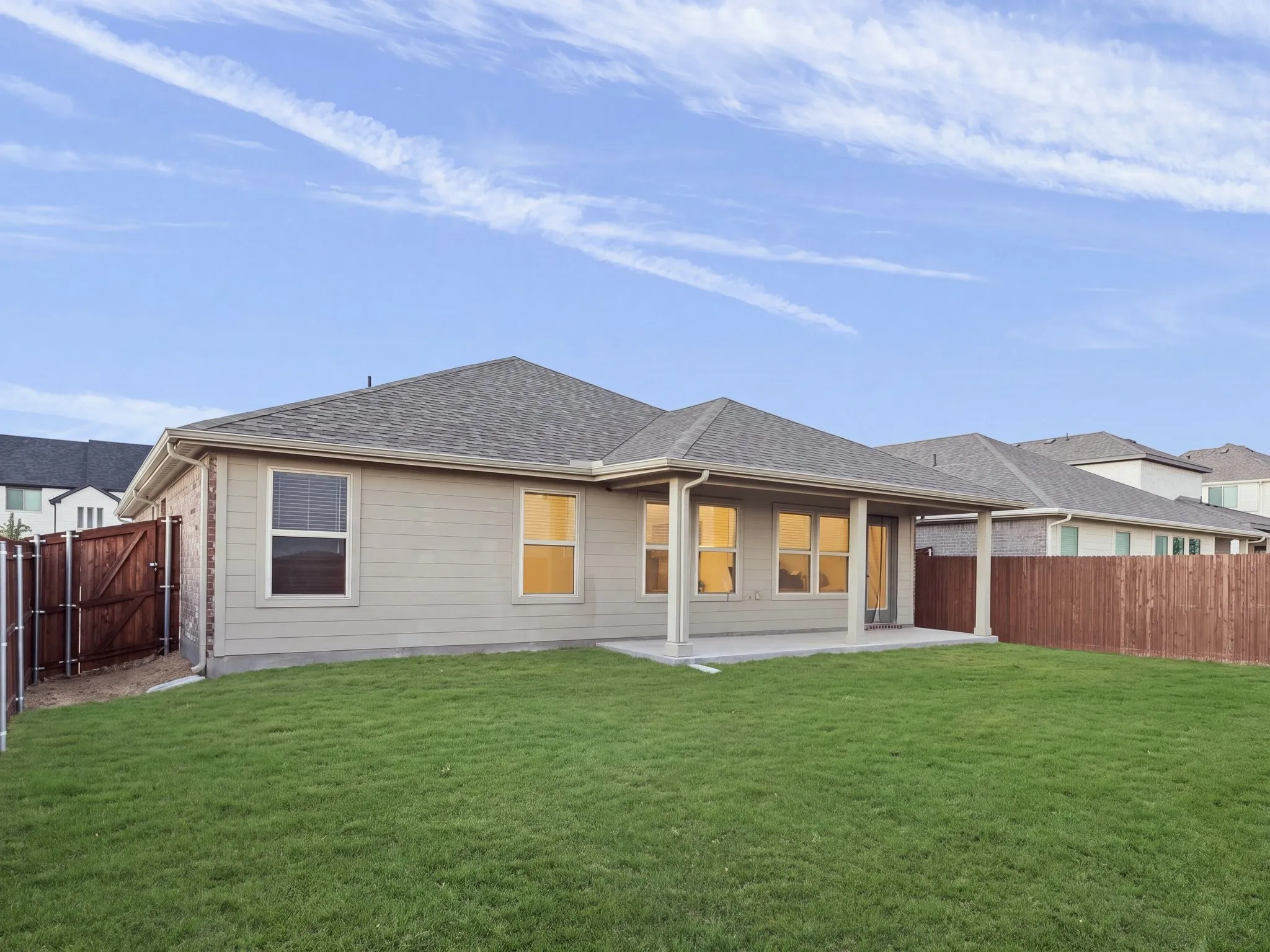 Expansive lawn with a covered patio, privacy fencing, and multiple windows