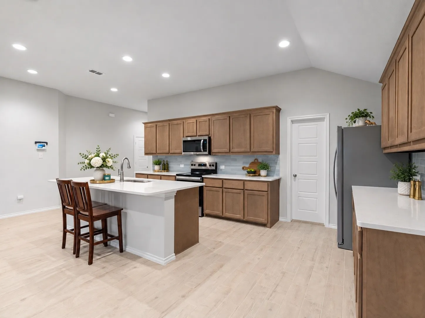 Kitchen featuring light wood-finish flooring, vaulted ceiling, recessed lighting, and a center island with a sink