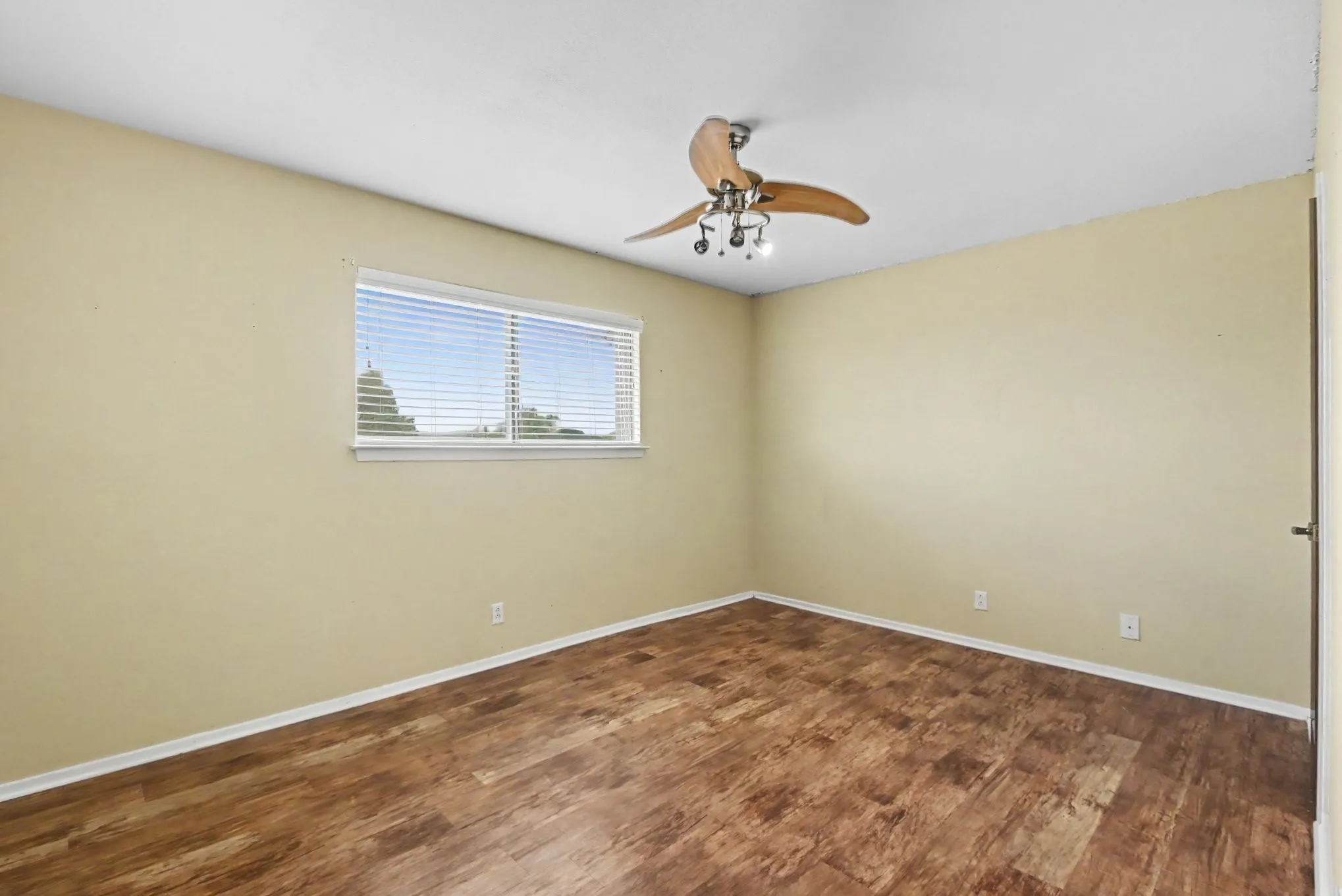 Wood-finish flooring, single window with blinds, ceiling fan with integrated lighting, and neutral wall tones