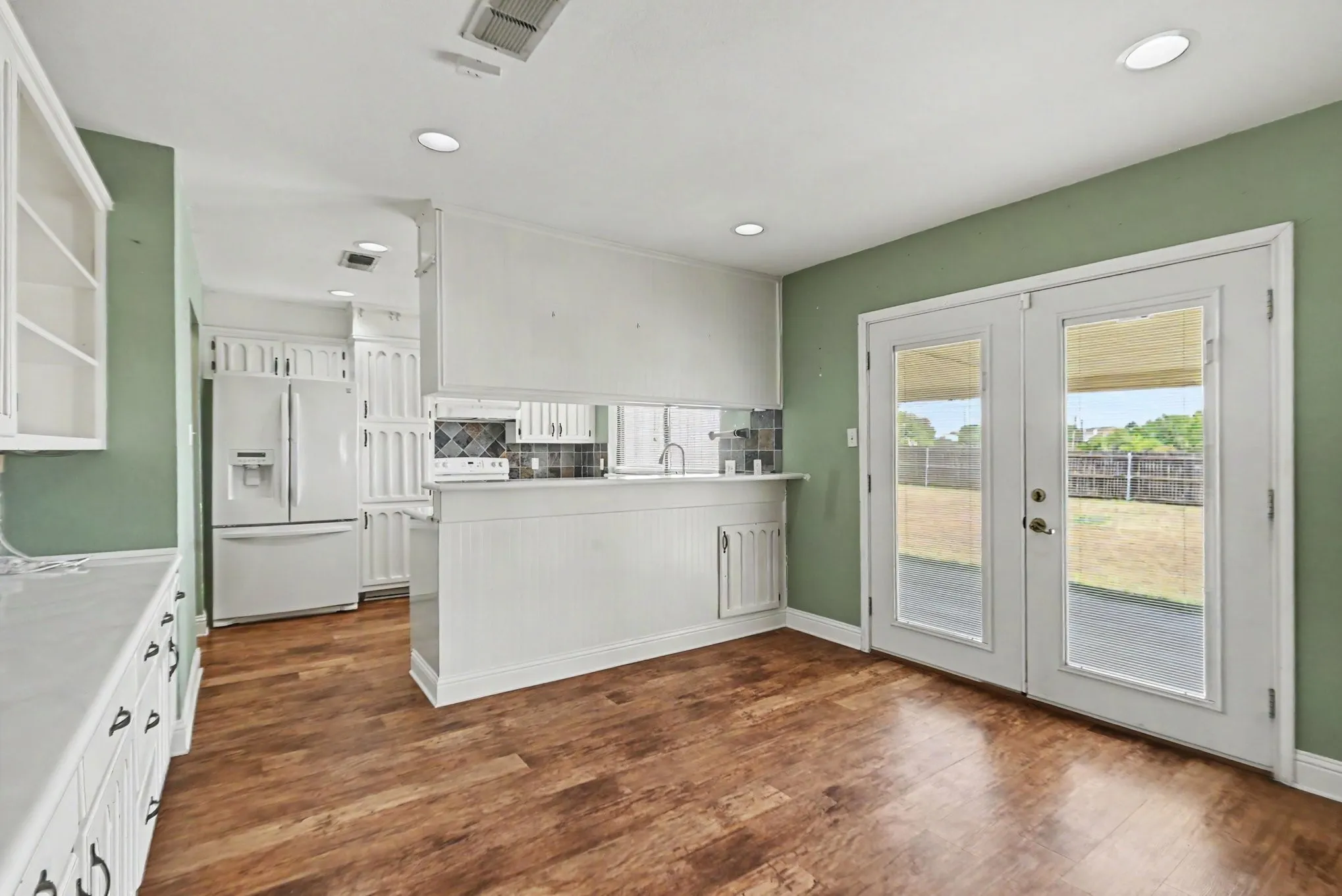 Wood-finish flooring, recessed lighting, white cabinetry, a built-in refrigerator, and double glass-panel doors