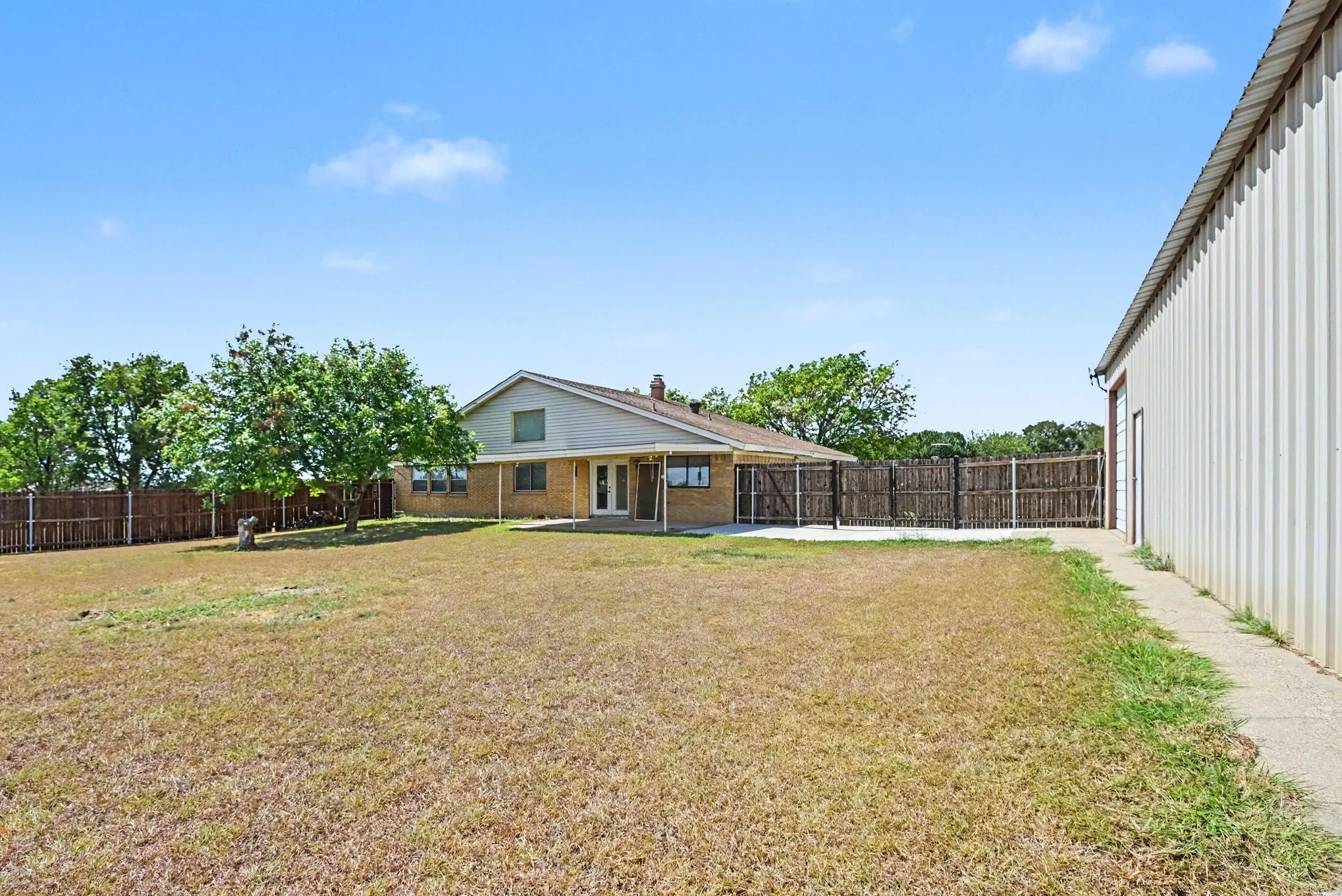 Expansive yard featuring a large detached metal building, concrete patio, and mature trees