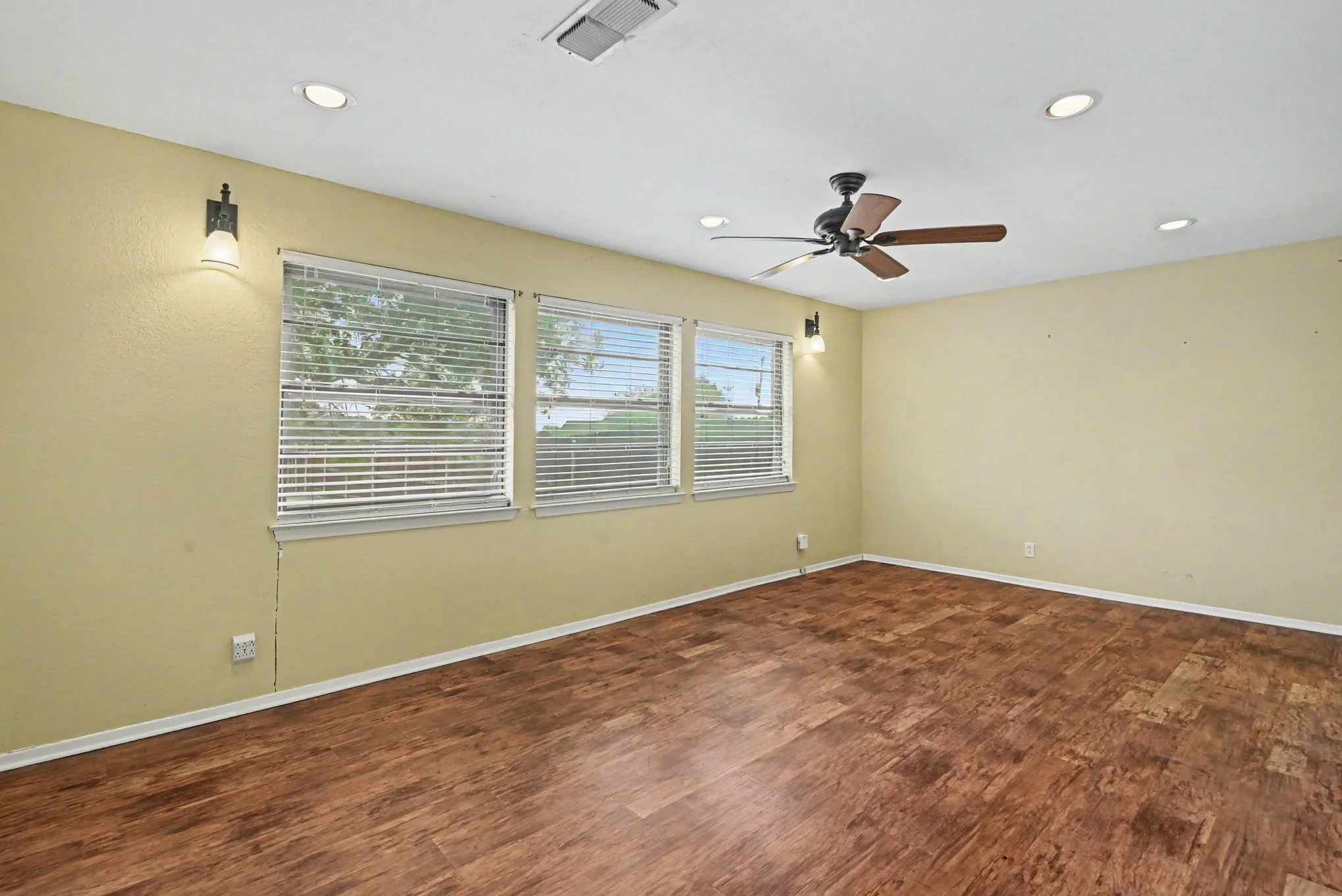 Recessed lighting, wood-finish flooring, ceiling fan, multiple windows with blinds, and wall-mounted sconces