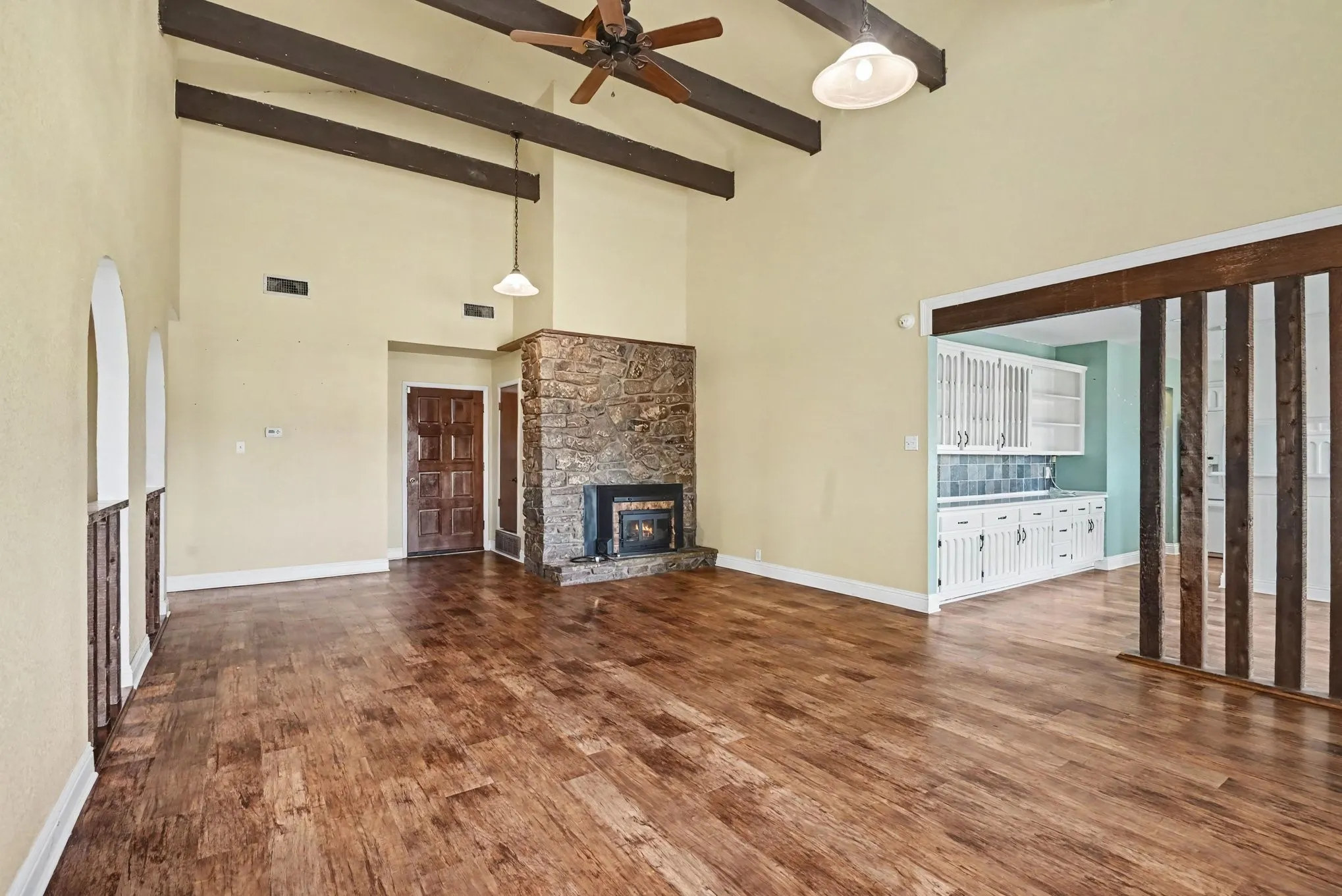 Vaulted ceiling with exposed wood beams, wood-finish flooring, stone fireplace, ceiling fan, and built-in cabinetry