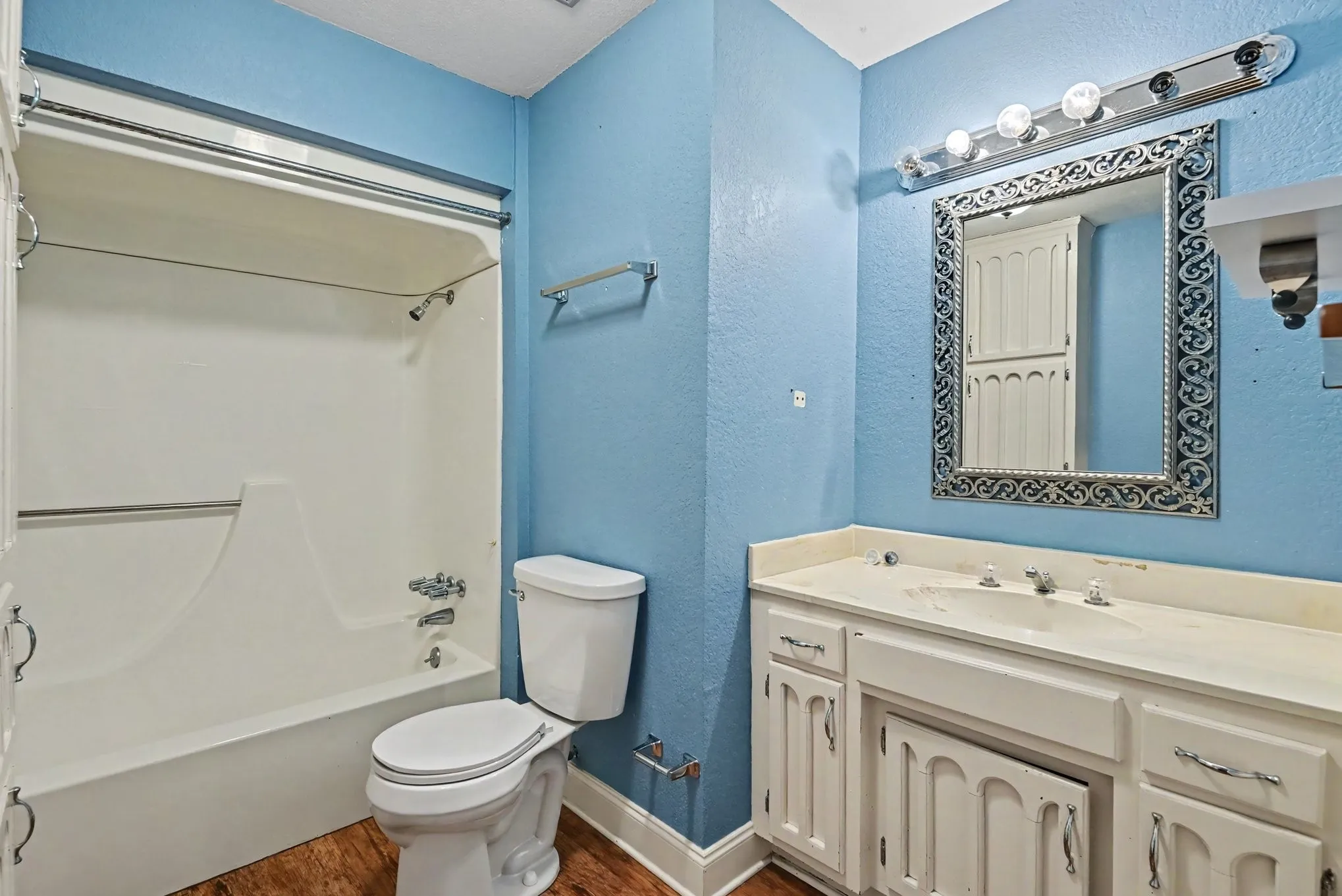 Bathroom featuring a shower/tub combination, single vanity with integrated sink, wood-finish flooring, and a decorative mirror
