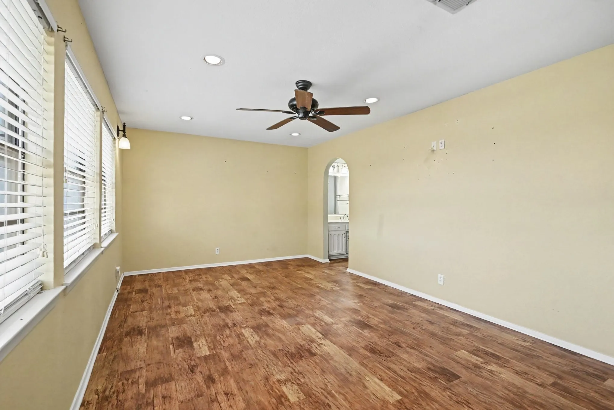 Wood-finish flooring, multiple windows with blinds, recessed ceiling lights, and a ceiling fan
