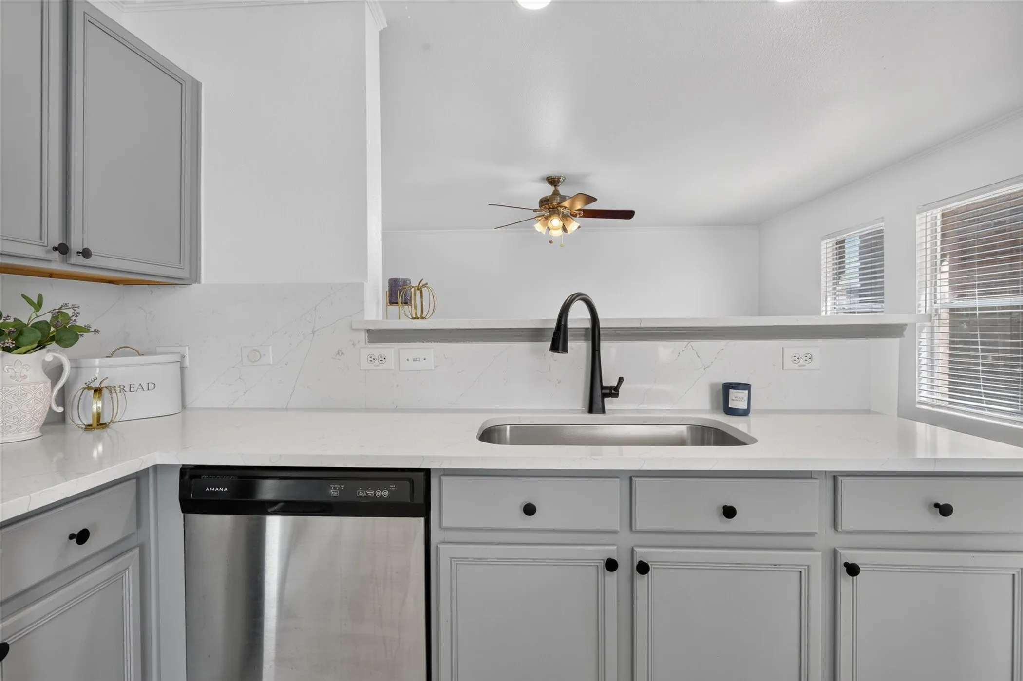 Light gray cabinetry with black hardware, stainless steel dishwasher, undermount sink, black gooseneck faucet, and white countertops