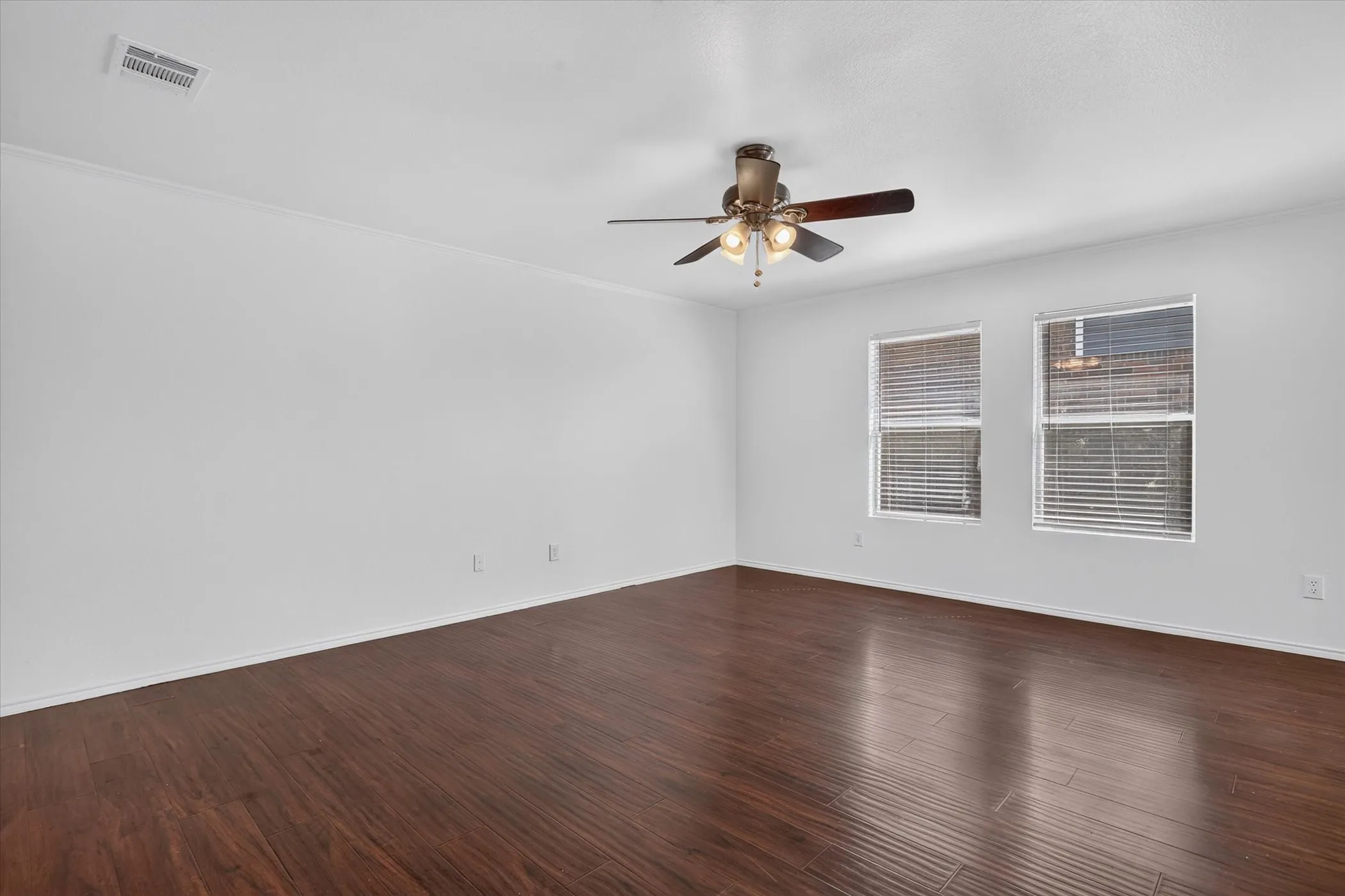Wood-finish flooring, bright white walls, crown molding, and two windows with blinds