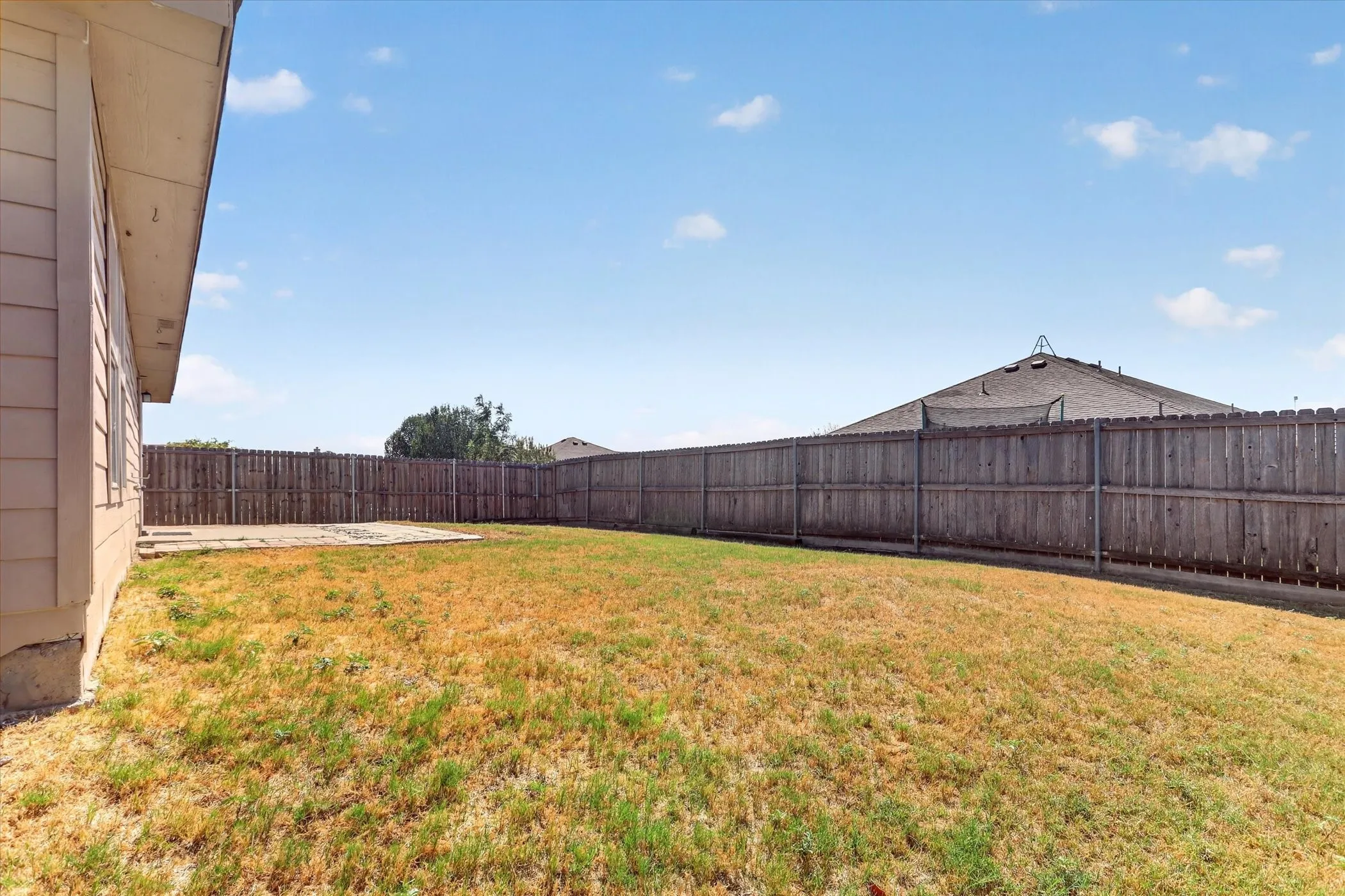 Expansive rear yard featuring a privacy fence, concrete patio, and mature landscaping