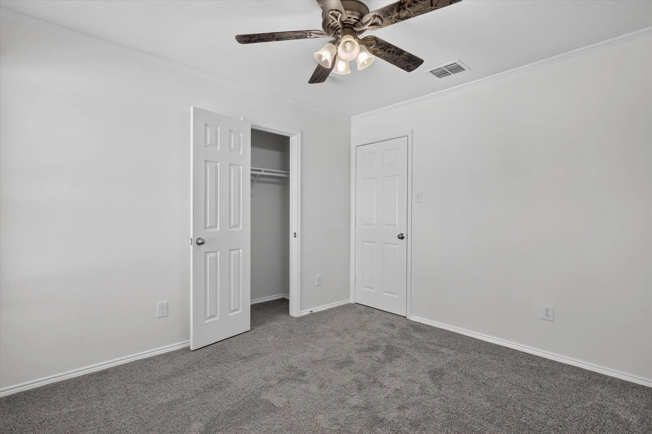 White painted walls with crown molding, gray carpeting, white paneled doors, and a ceiling fan with integrated lighting