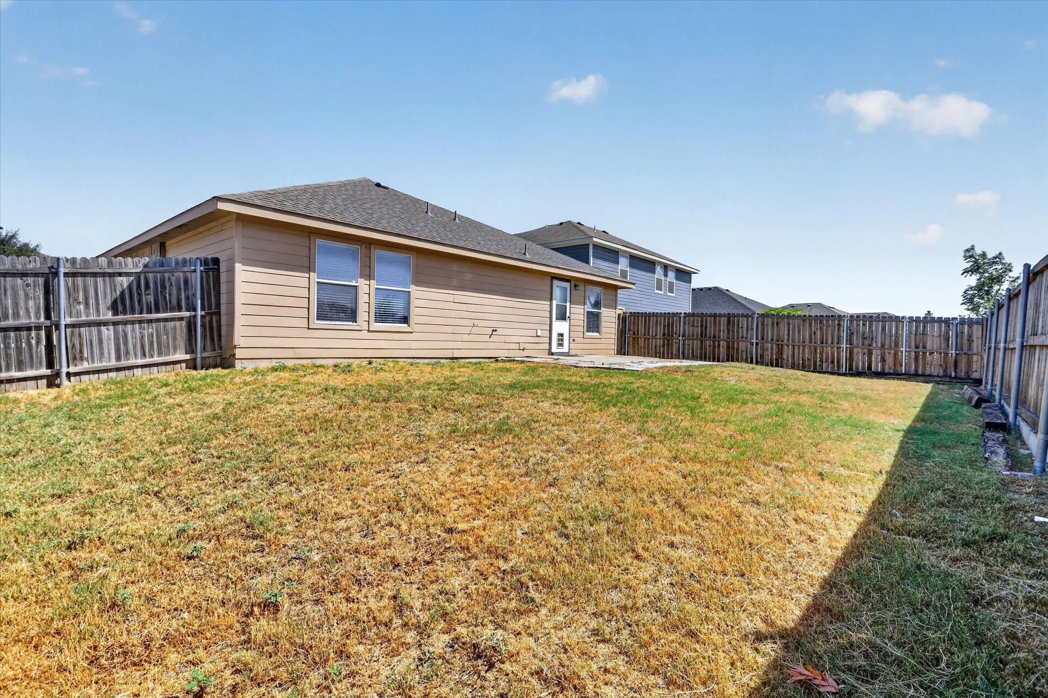 Expansive fenced backyard featuring a concrete patio and a residential structure with horizontal siding