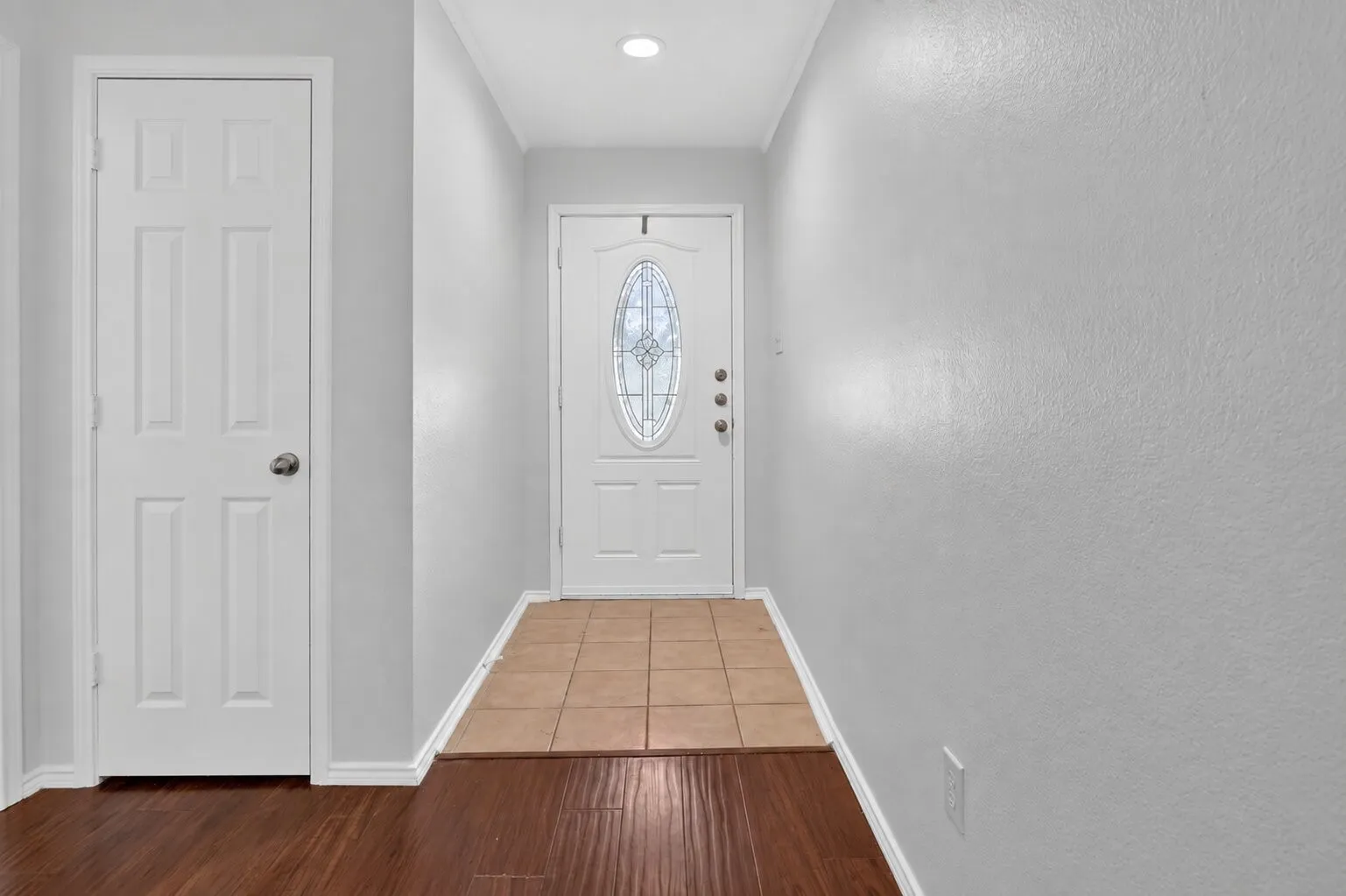 Welcoming entryway featuring a six-panel interior door, glazed entry door with decorative oval glass insert, recessed ceiling lighting, and mixed wood-finish flooring with warm brown tones throughout
