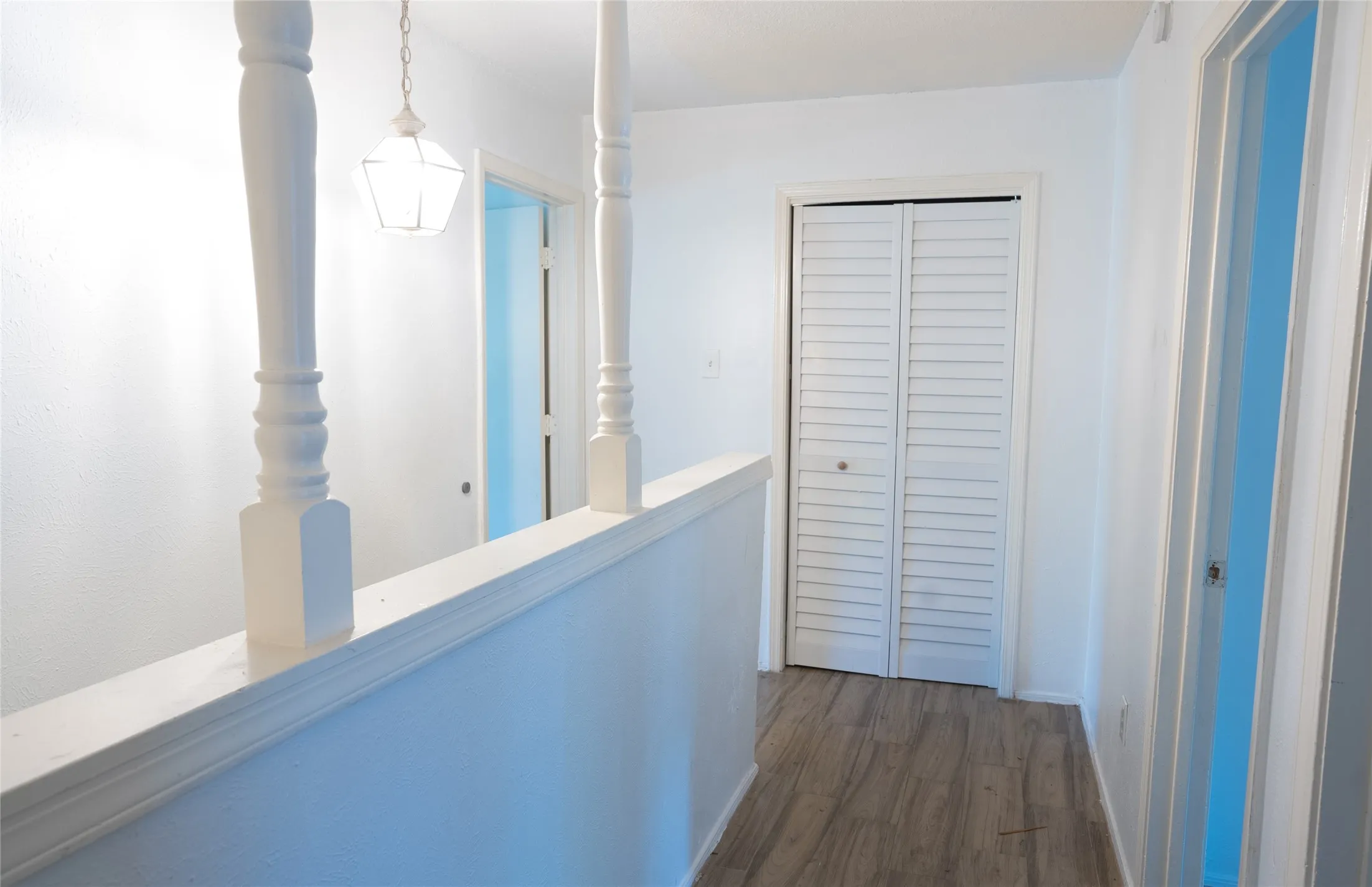 Wood-finish flooring, white walls, white louvered closet doors, and a decorative pendant light fixture