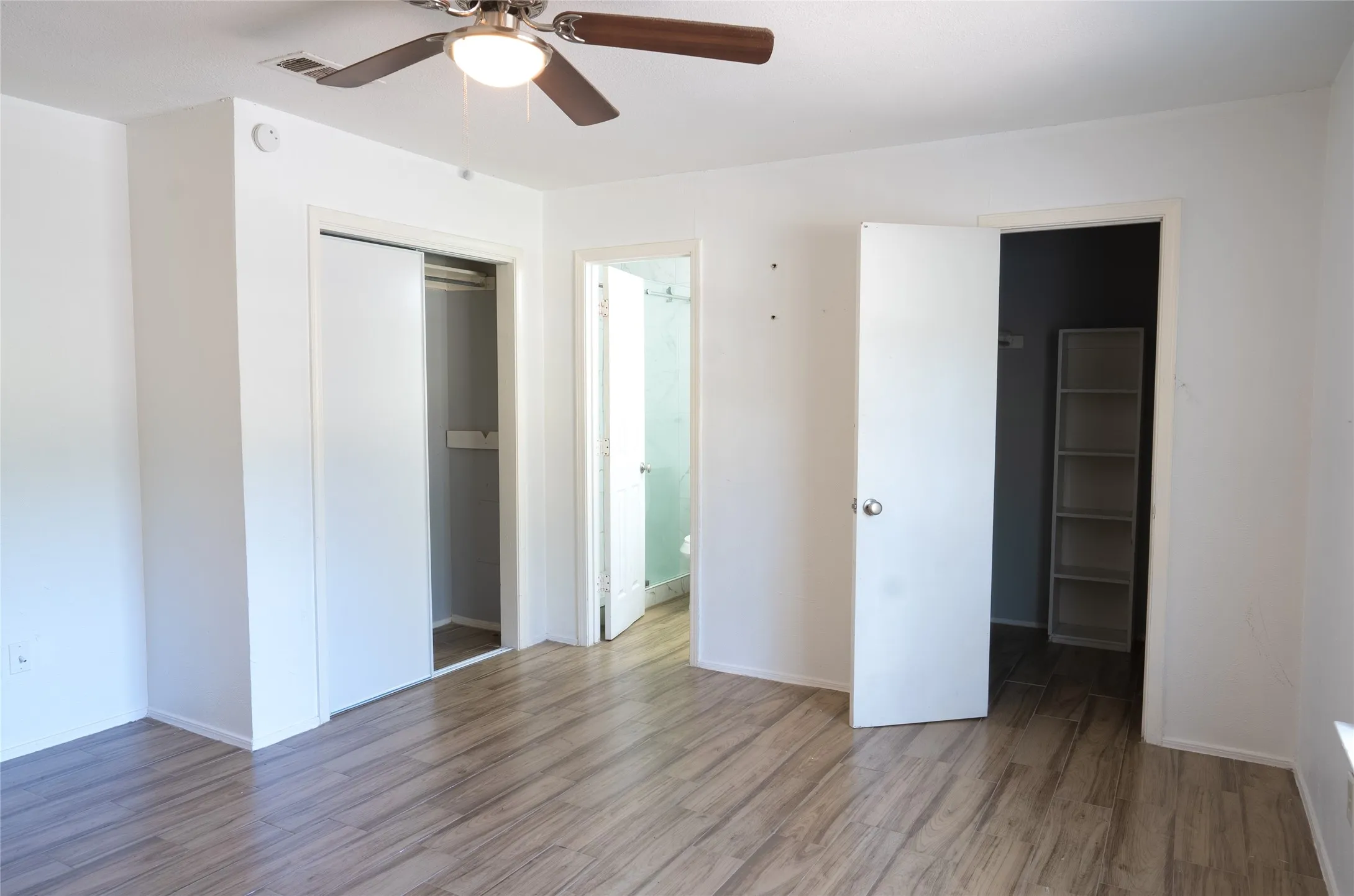 Wood-finish flooring, ceiling fan with light fixture, and two closets with sliding doors