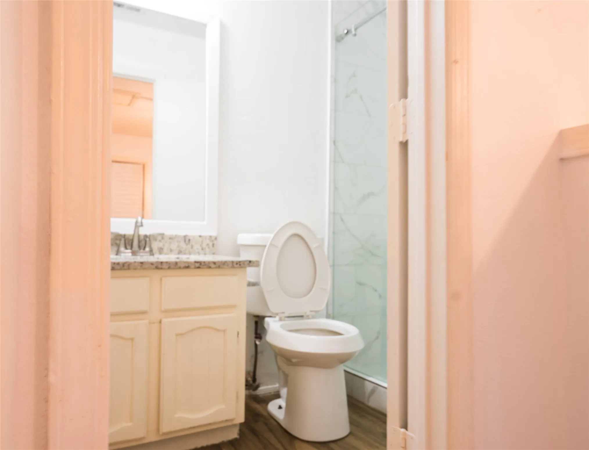 Vanity with a granite-style countertop, wood-finish flooring, and a glass-enclosed shower with a tiled surround