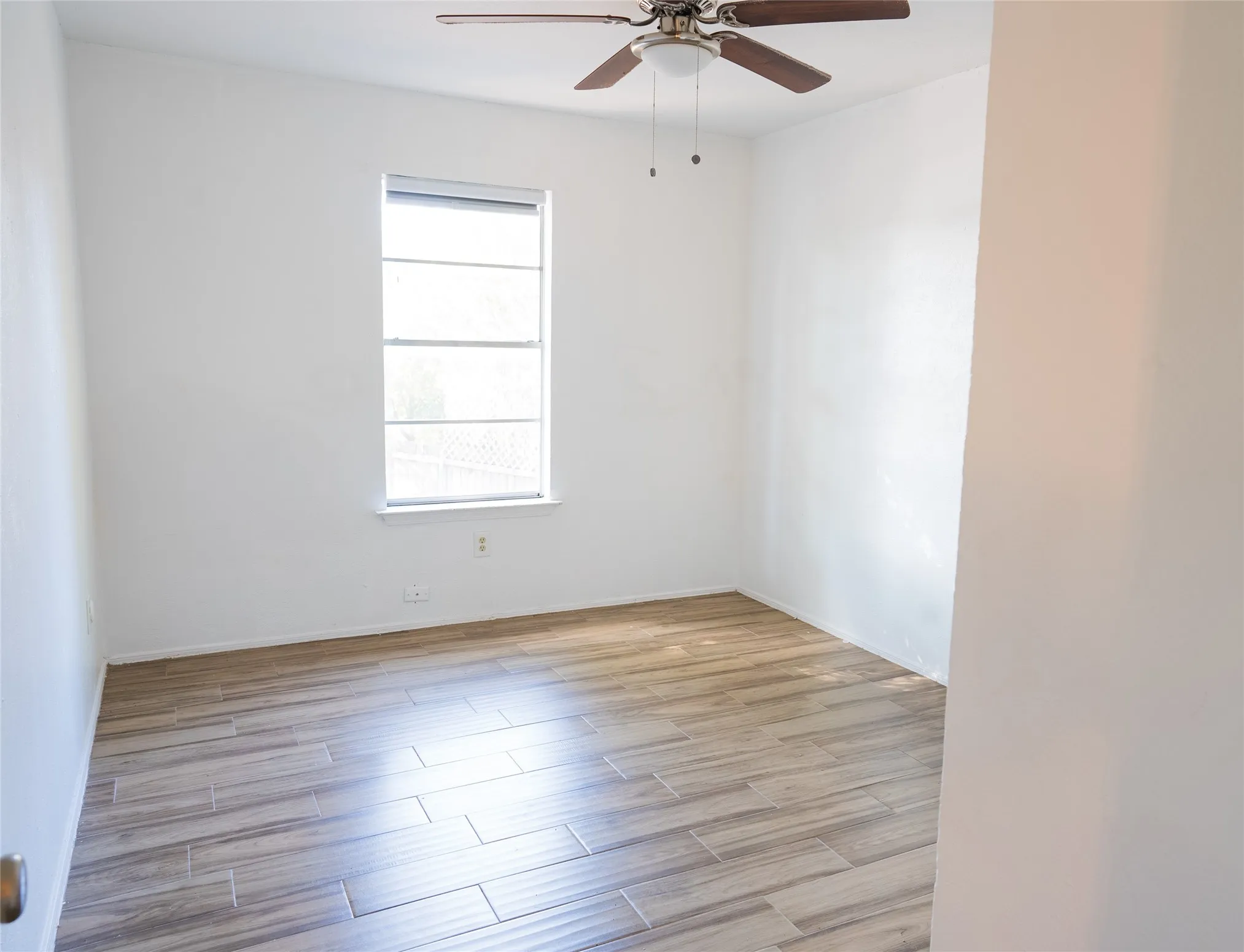 Wood-finish plank flooring, ceiling fan with integrated lighting, and a single window with horizontal blinds