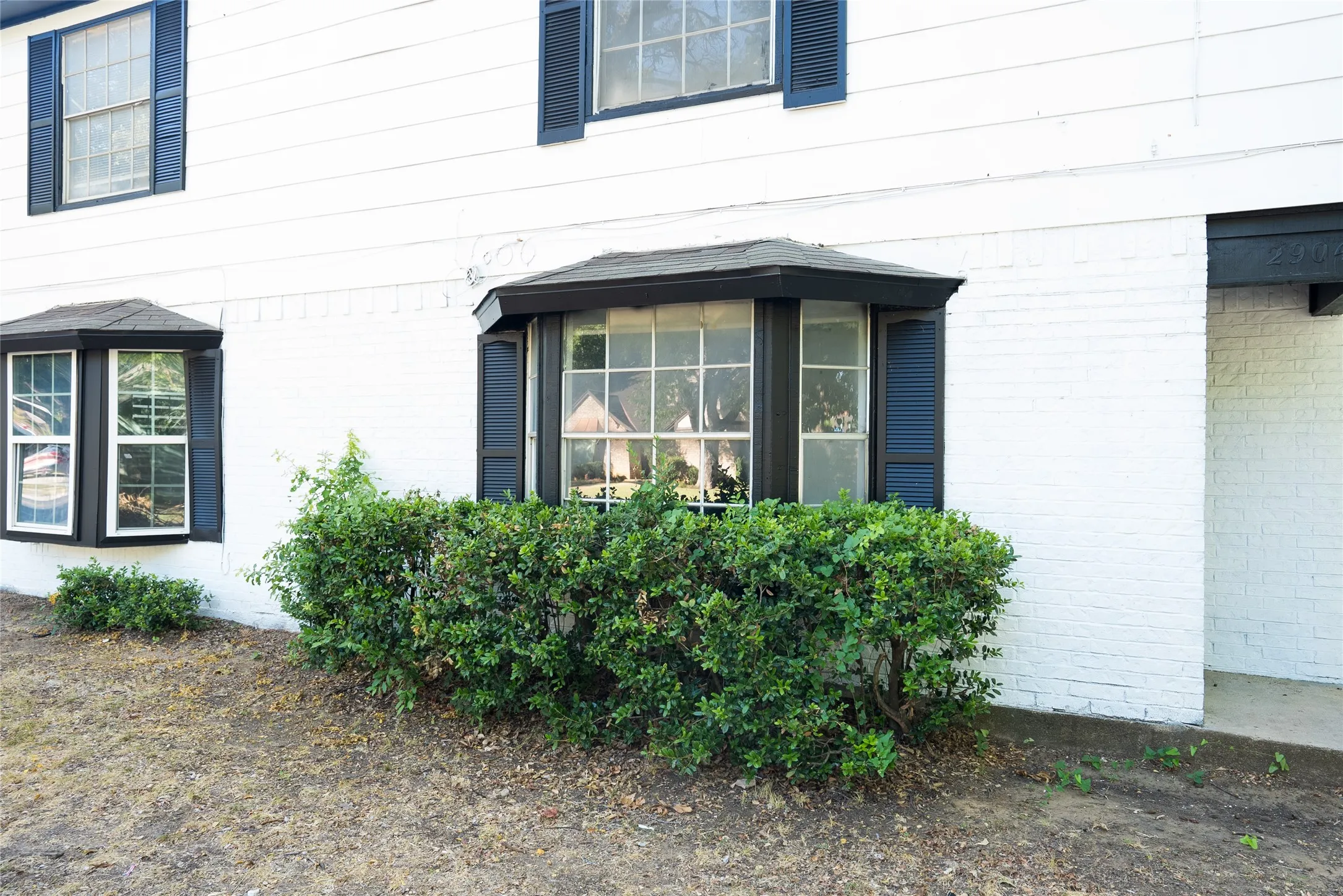 White painted brick facade with bay windows, dark window frames, and dark louvered shutters