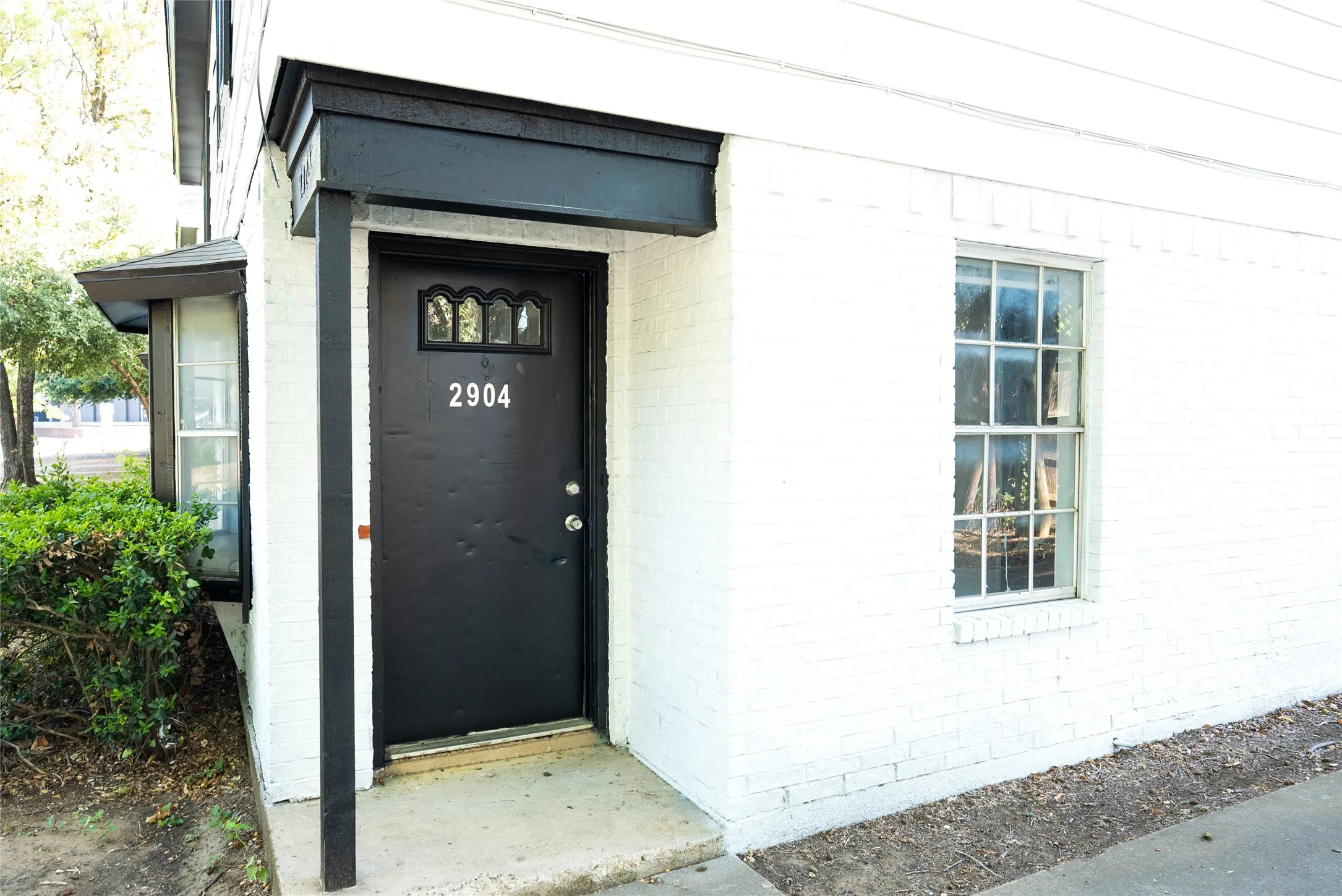 White painted brick exterior with a black entry door, decorative transom, and address numerals