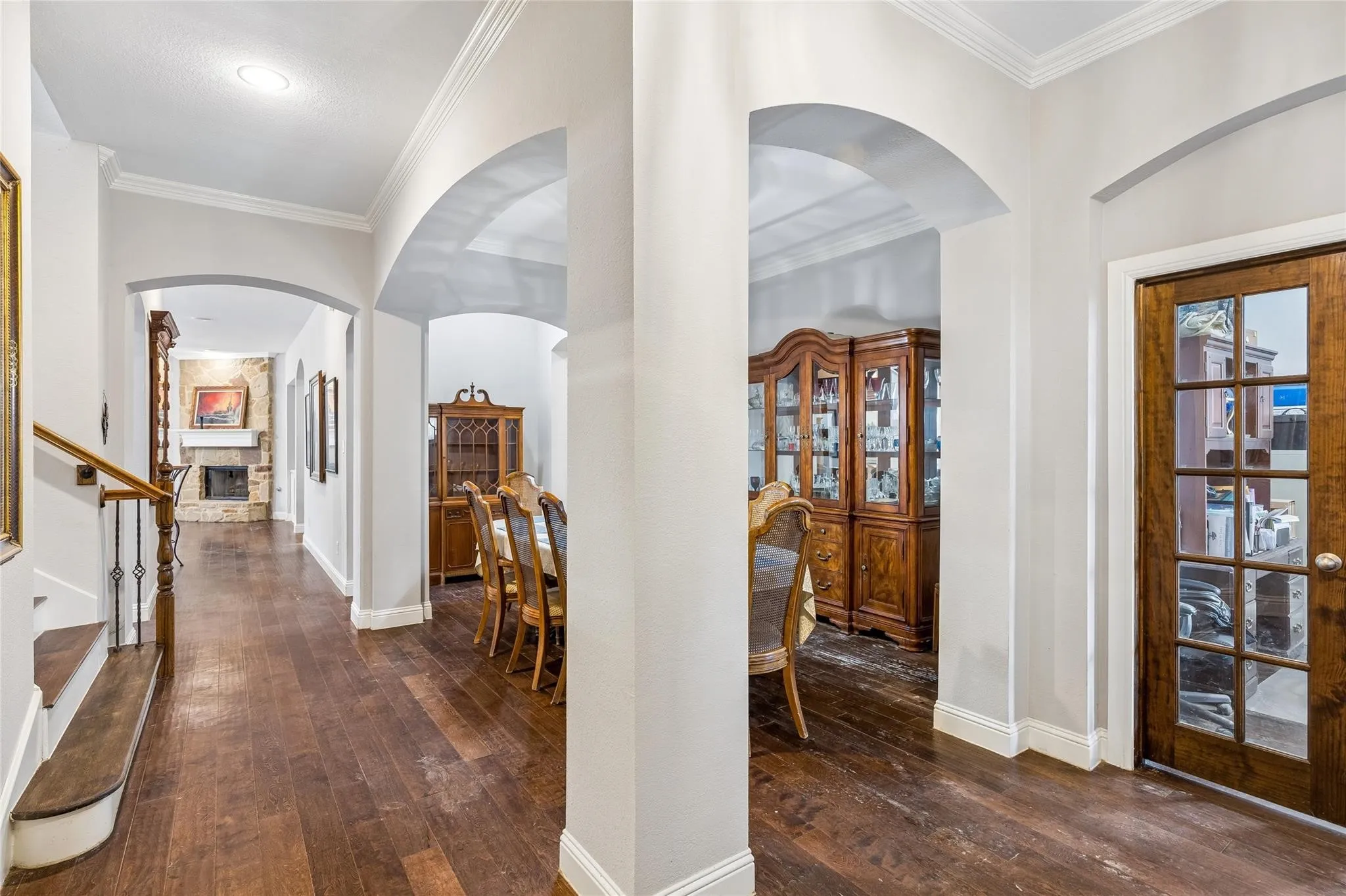 Wood-finish flooring throughout, multiple arched doorways, crown molding, and a wood-paneled door with glass inserts