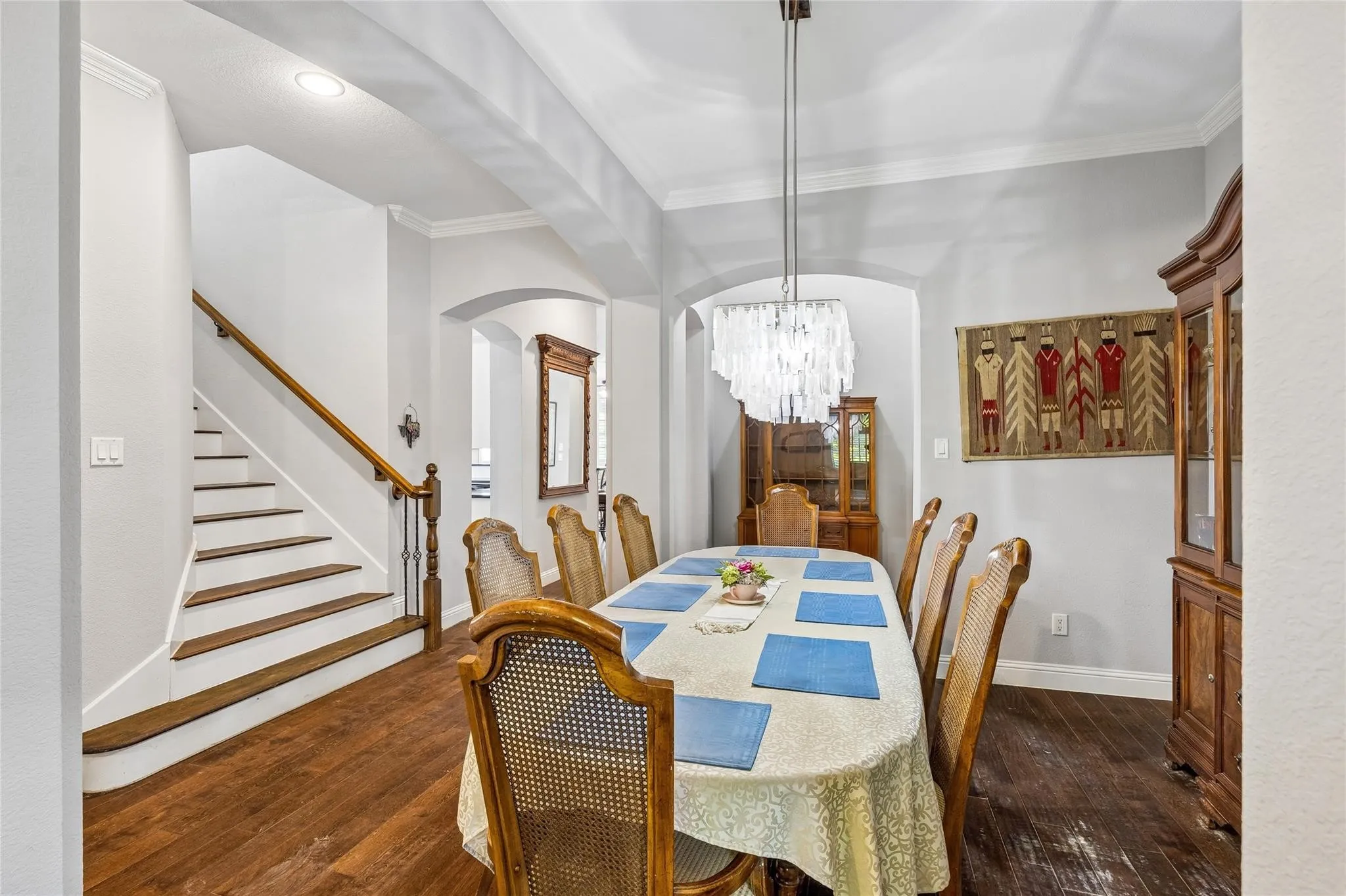 Wood-finish flooring, staircase with wood handrail, crown molding, arched entryways, and a chandelier with a layered design