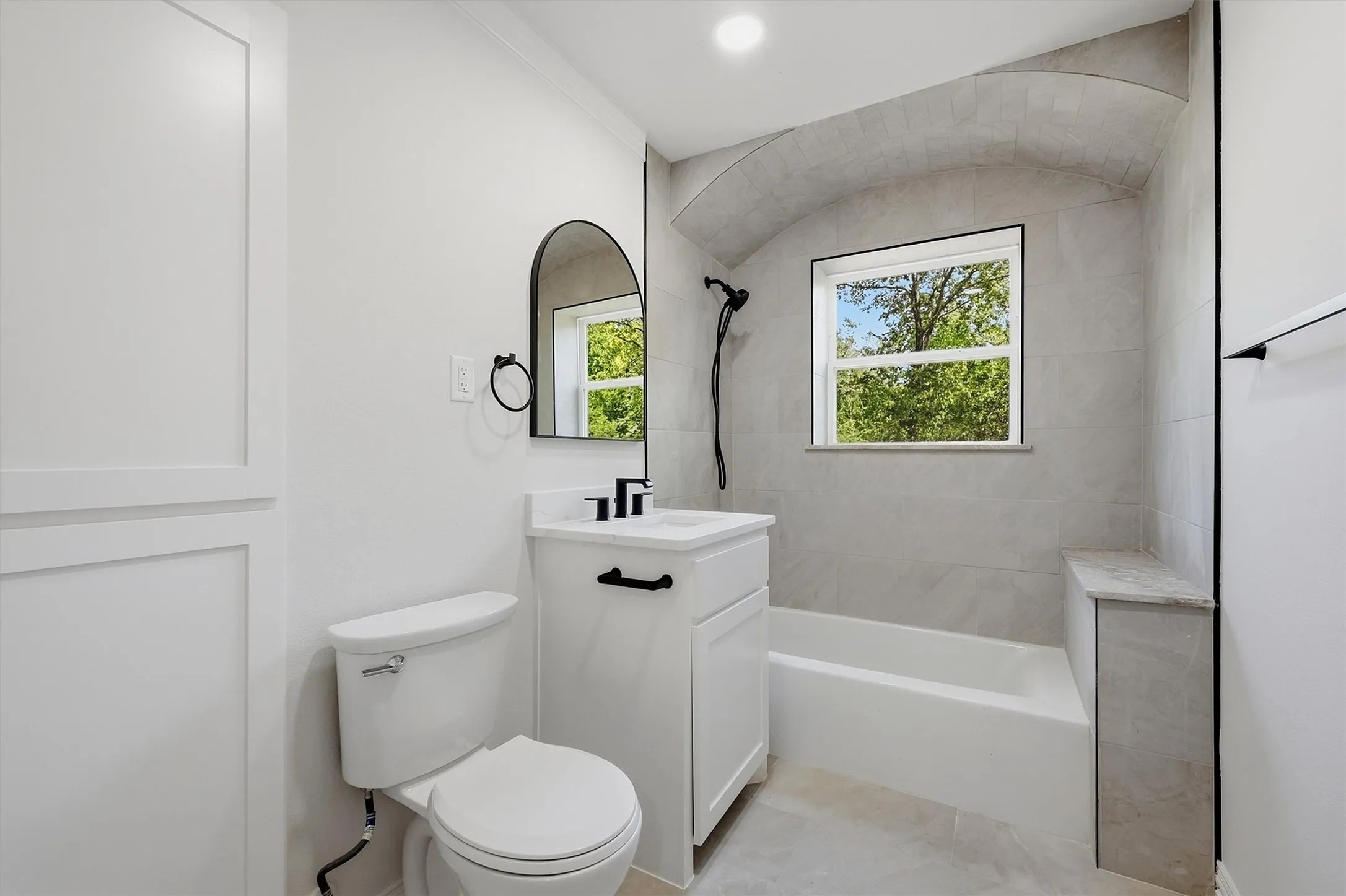 Modern bathroom featuring a white vanity with black hardware, a tiled tub surround, and a built-in shower bench