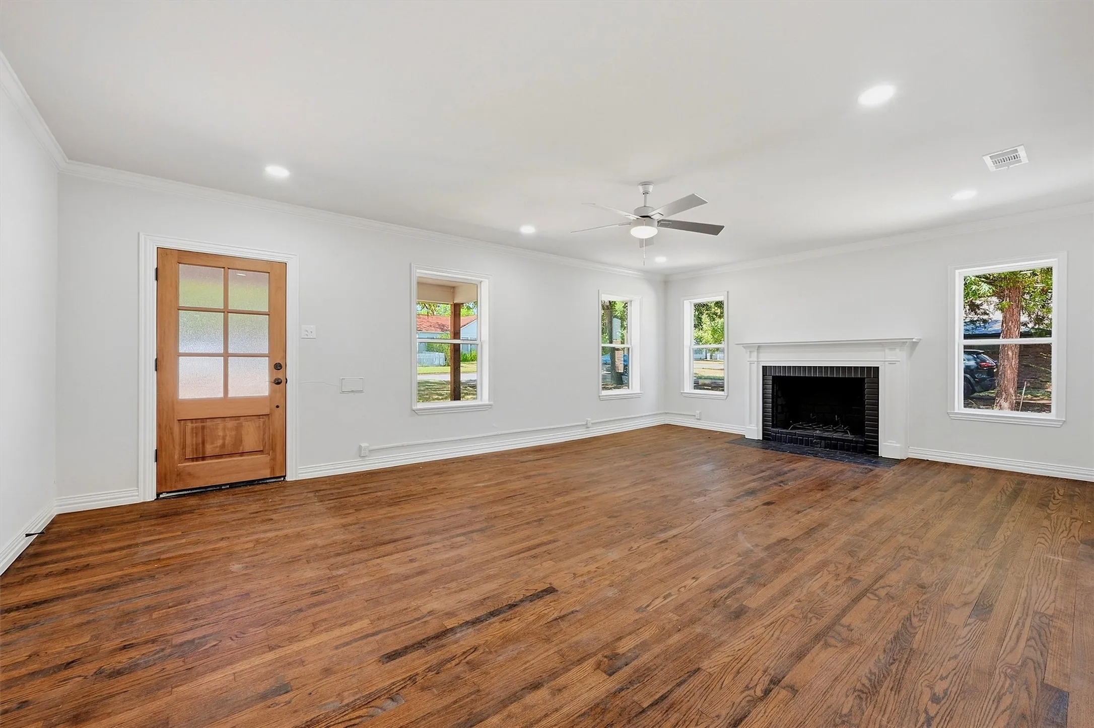 Hardwood flooring, recessed lighting, ceiling fan, decorative fireplace with mantel, and multiple windows