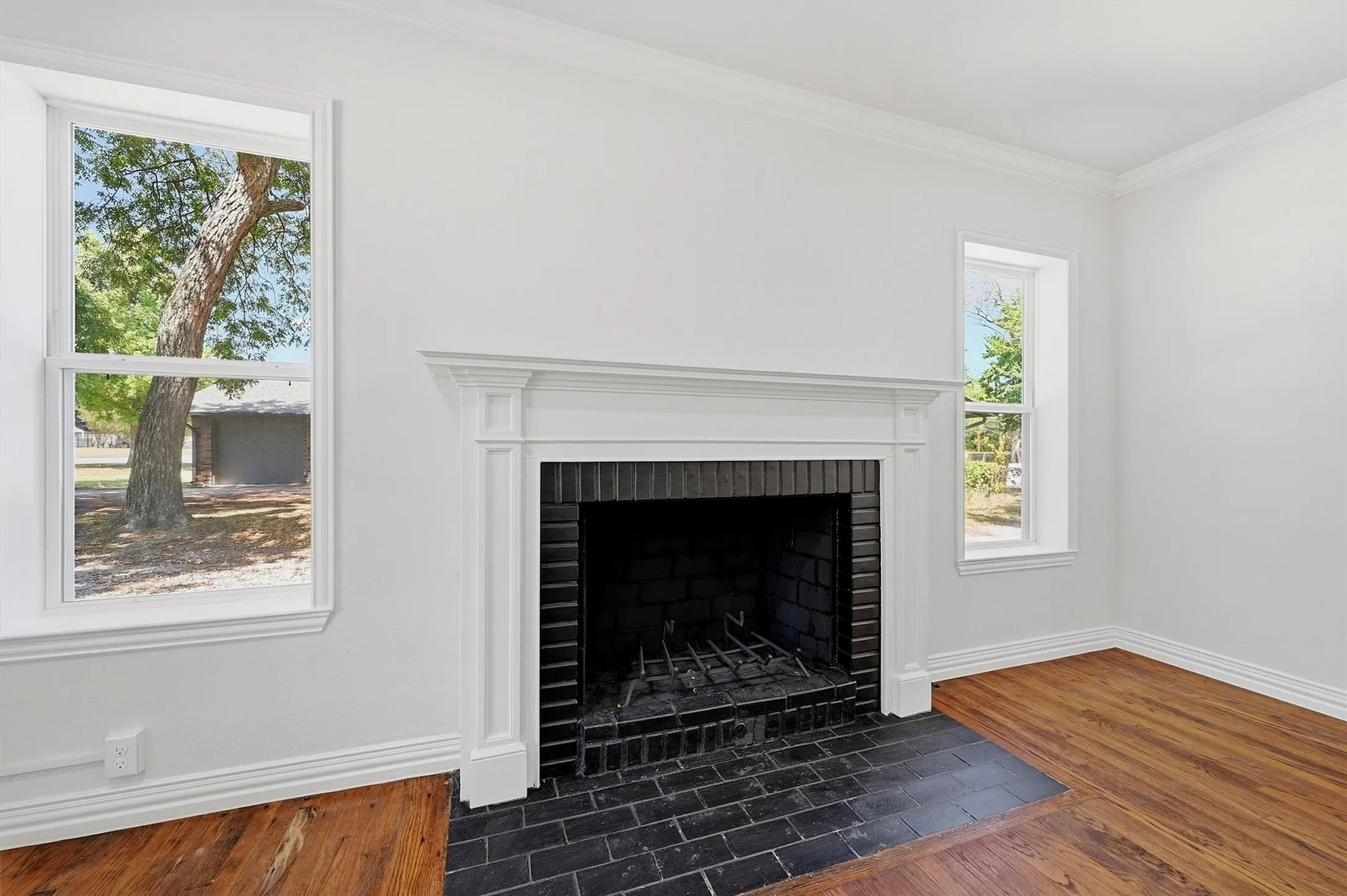 White-painted walls and trim with crown molding, wood-finish flooring, and a fireplace with a black brick firebox and hearth