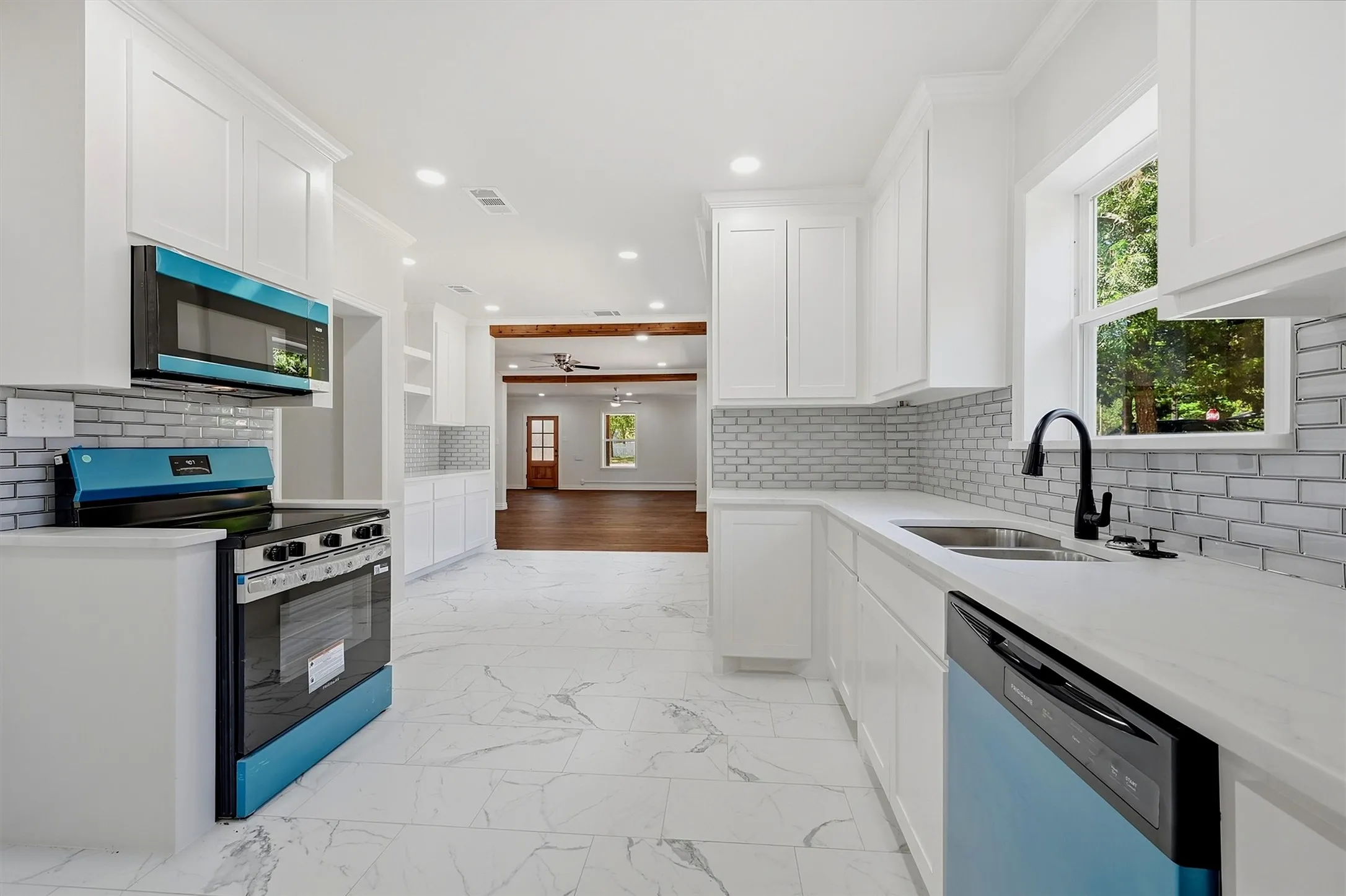 White cabinetry, white countertops, subway tile backsplash, stainless steel sink, and wood-finish flooring in the background