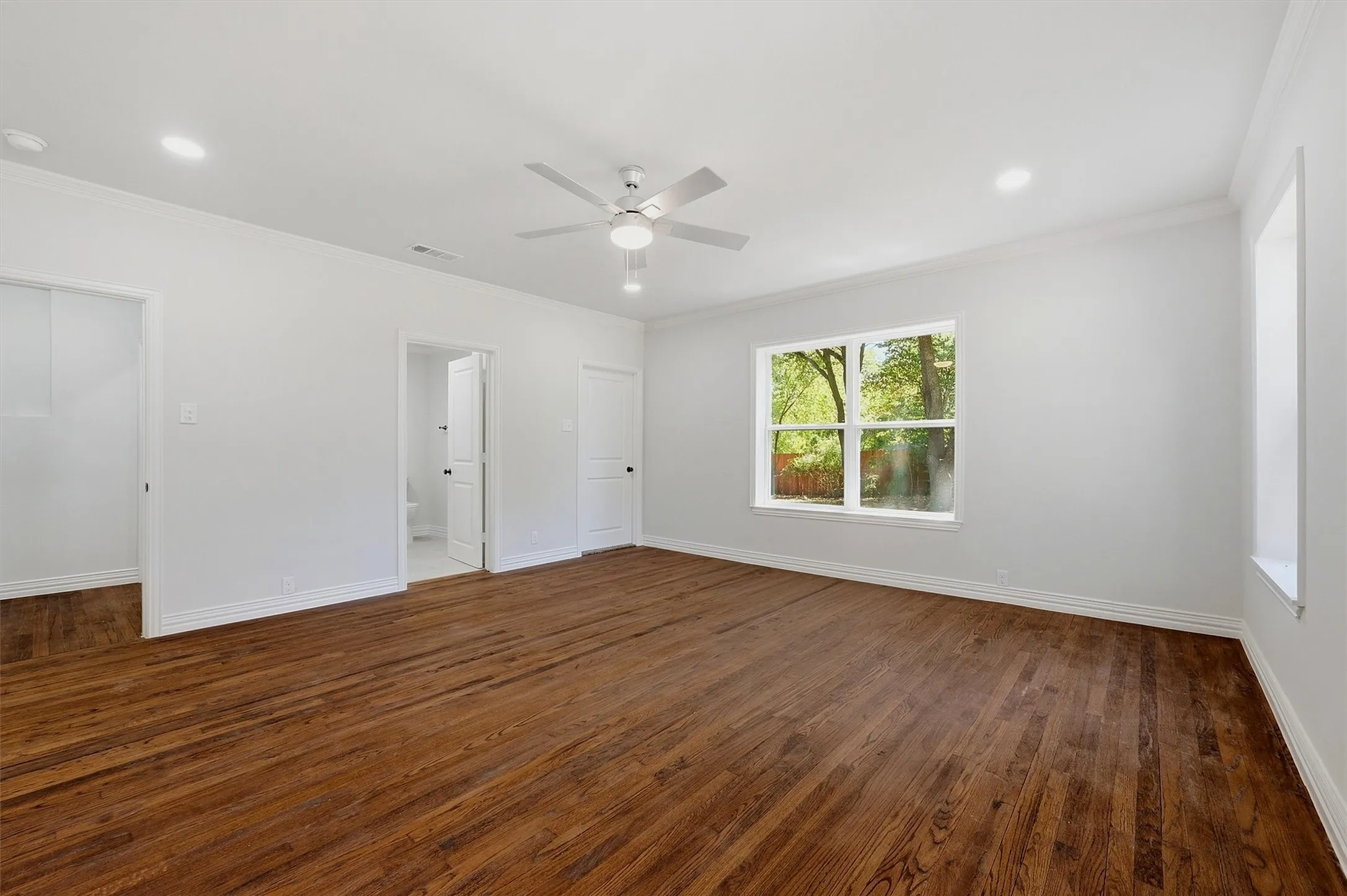 Spacious room featuring wood-finish flooring, recessed lighting, a ceiling fan, and a large window with white trim