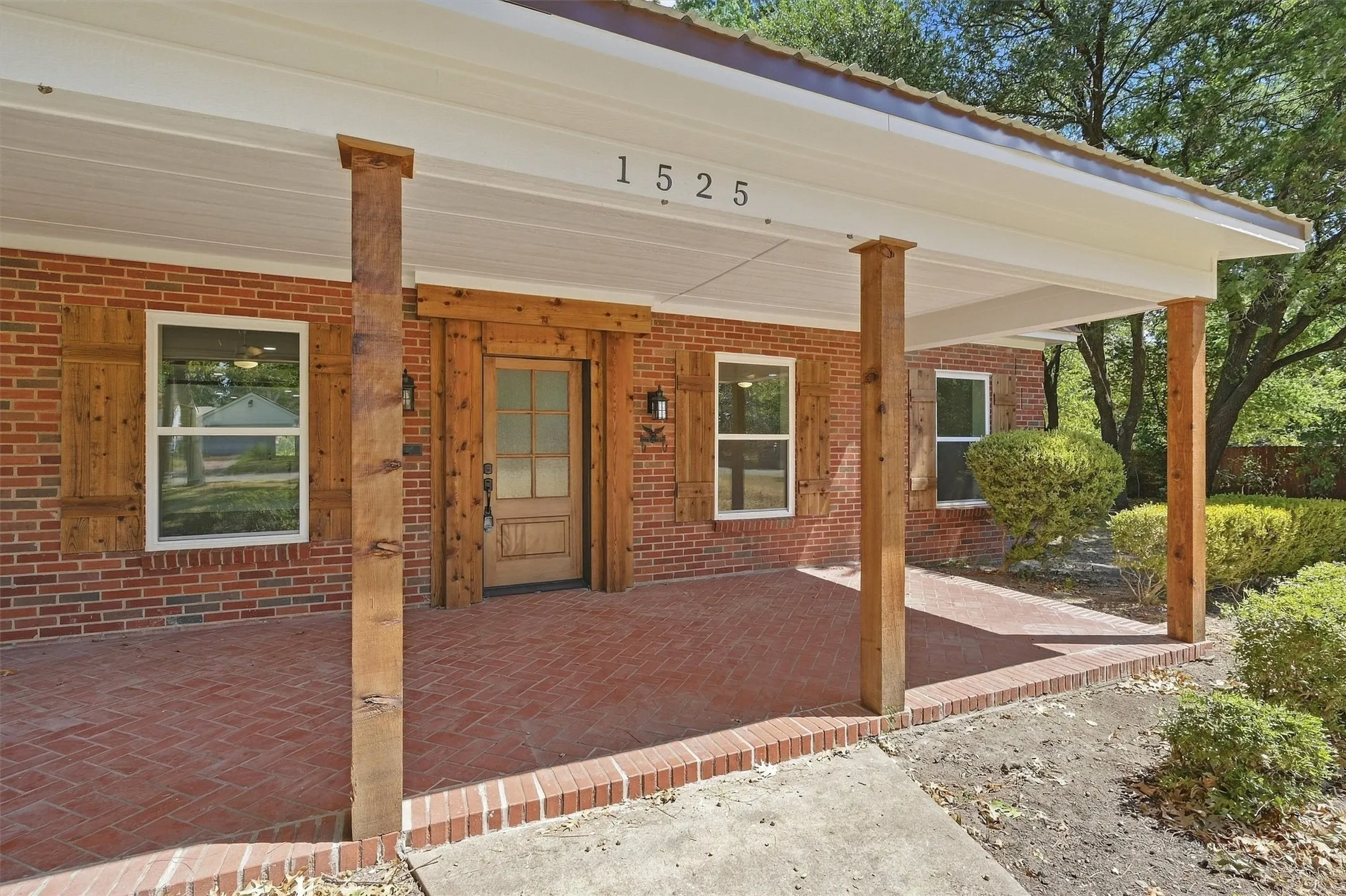 Brick exterior with wood shutters, covered porch with exposed wood posts, and a brick-patterned hardscaping