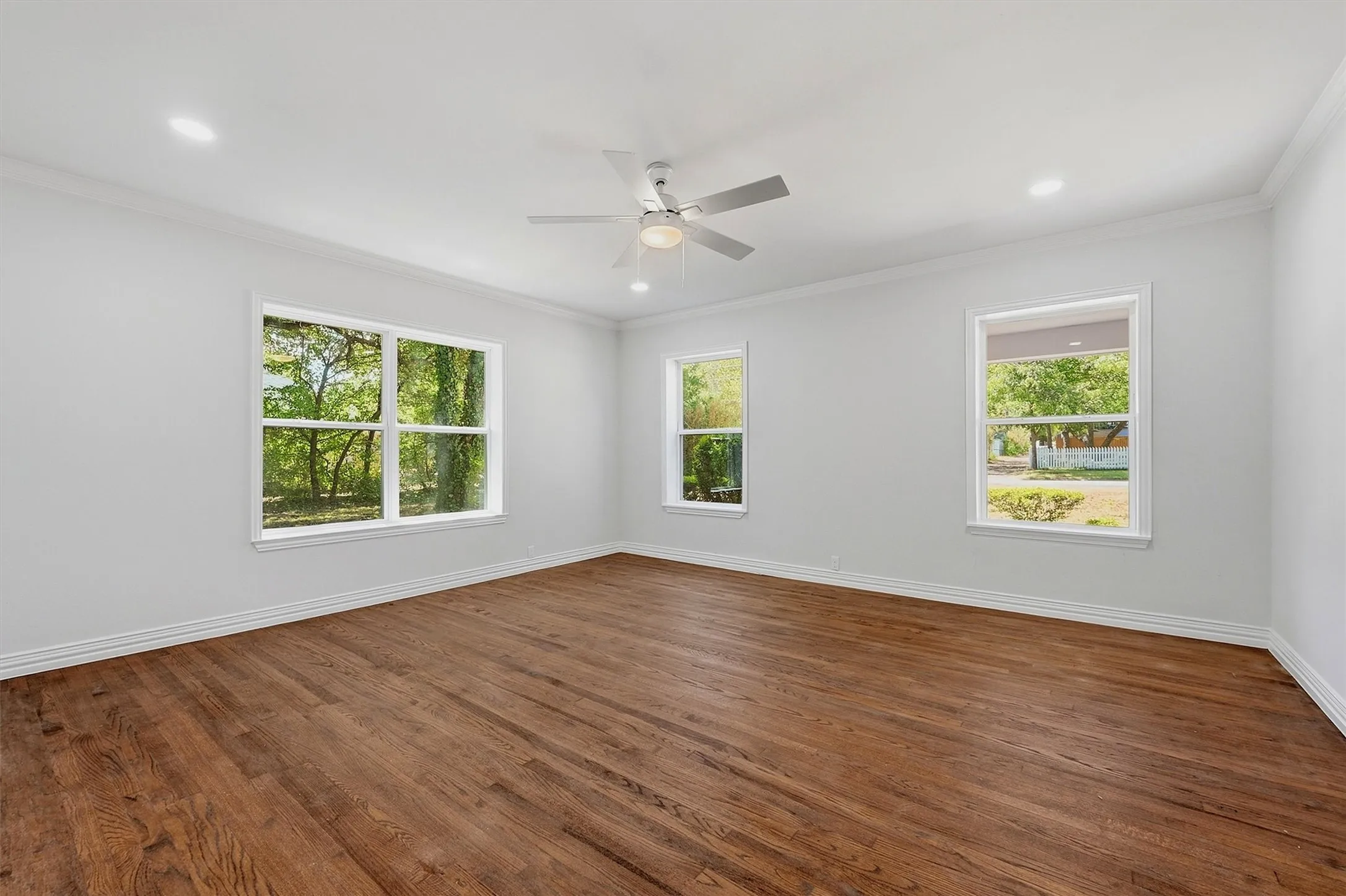 Spacious room featuring wood-finish flooring, recessed lighting, a ceiling fan, and multiple windows