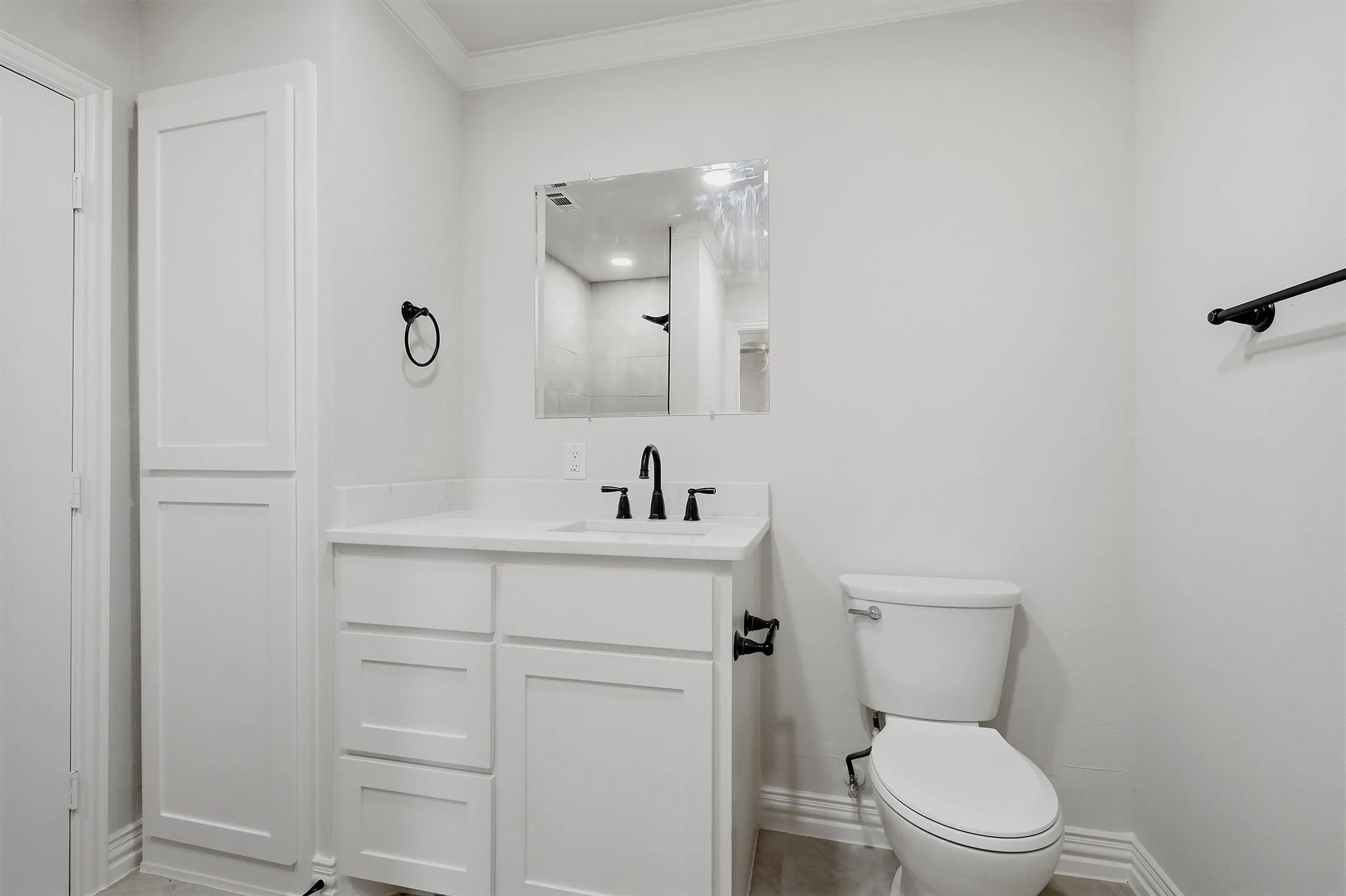 White vanity with integrated sink, matte black fixtures, framed mirror, and built-in linen cabinet